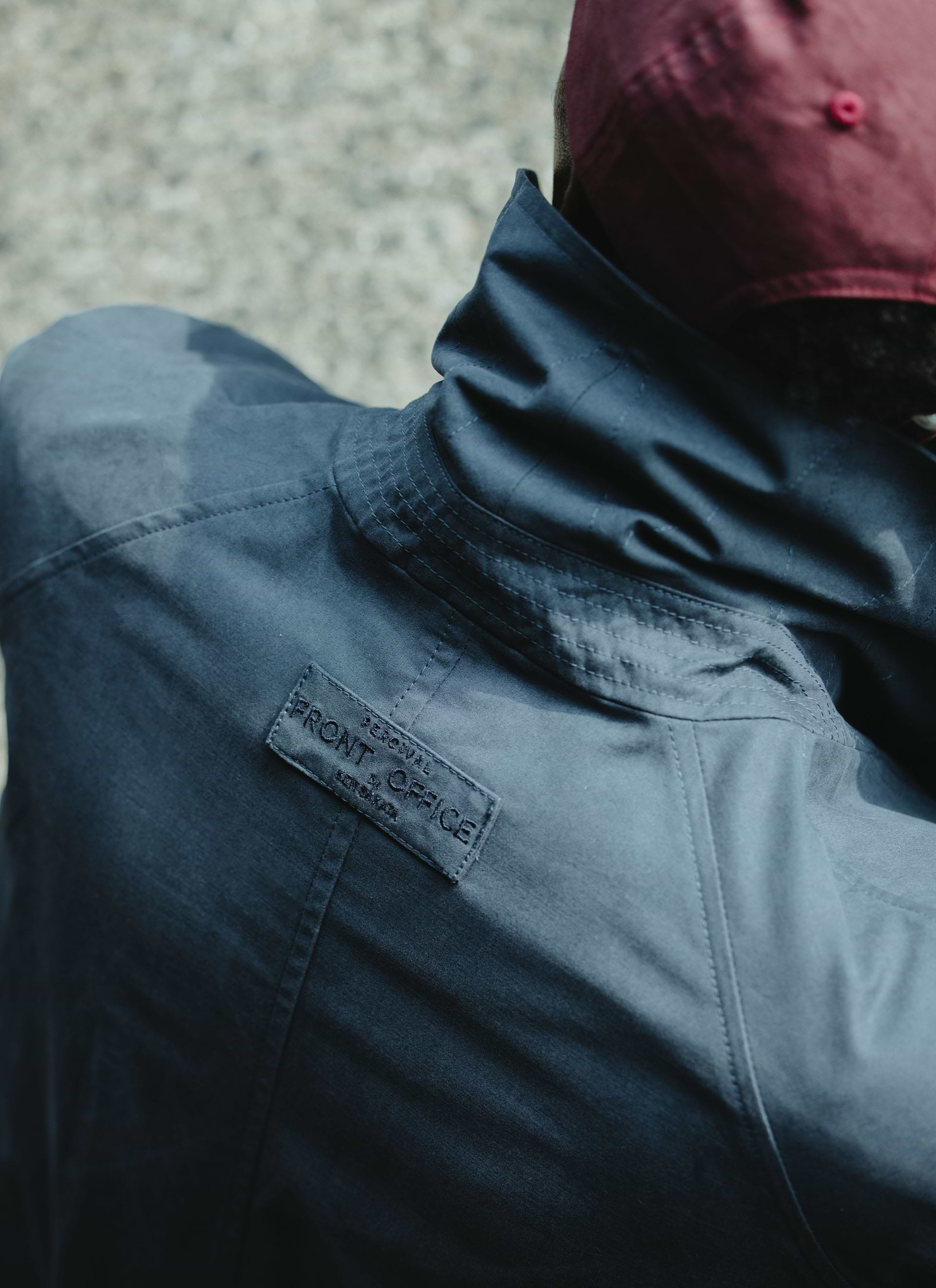 Close-up of the embroidered collaboration tab on the navy Percival x Front Office peached cotton Mac trench coat.