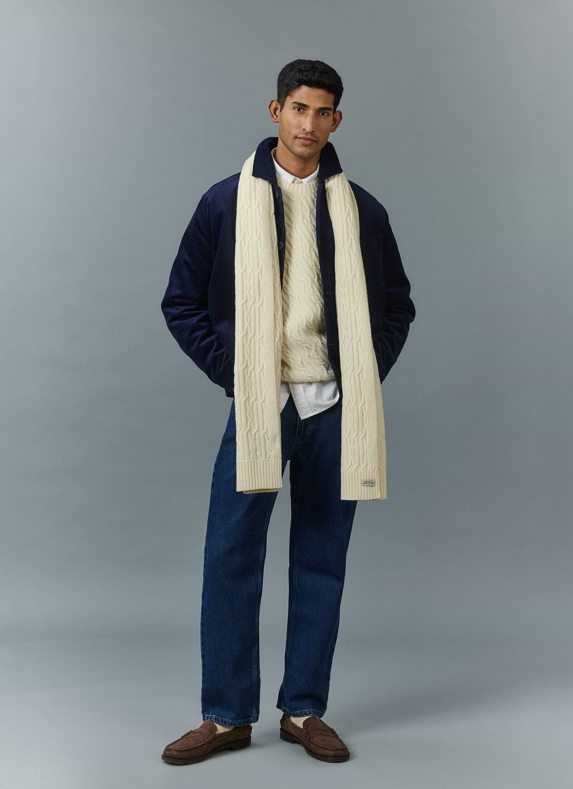 A model wears a Percival navy cord overshirt, ecru cable knit jumper and matching scarf, styled with dark denim jeans.