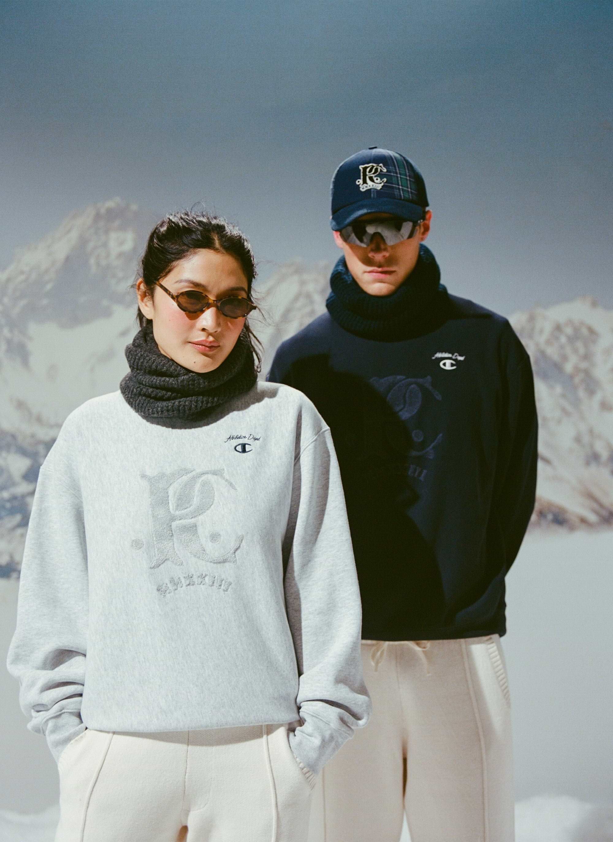 Two models showcase the Champion x Percival collaboration, wearing the navy and grey Chenille Patch sweatshirts for Percival.