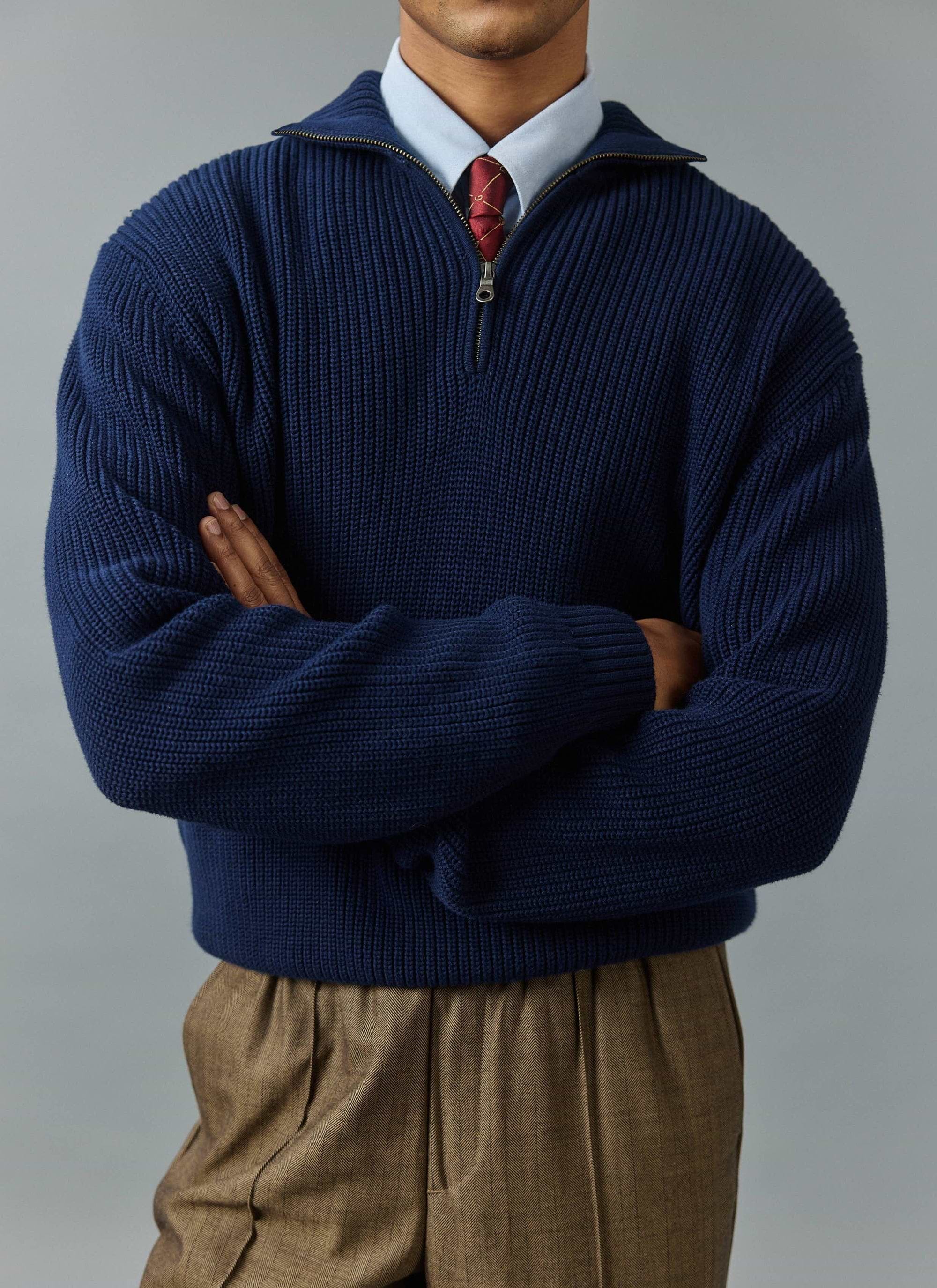 A man models the Percival Meyer Quarter Zip Fisherman jumper in blue, layered over a shirt and tie against a grey backdrop.