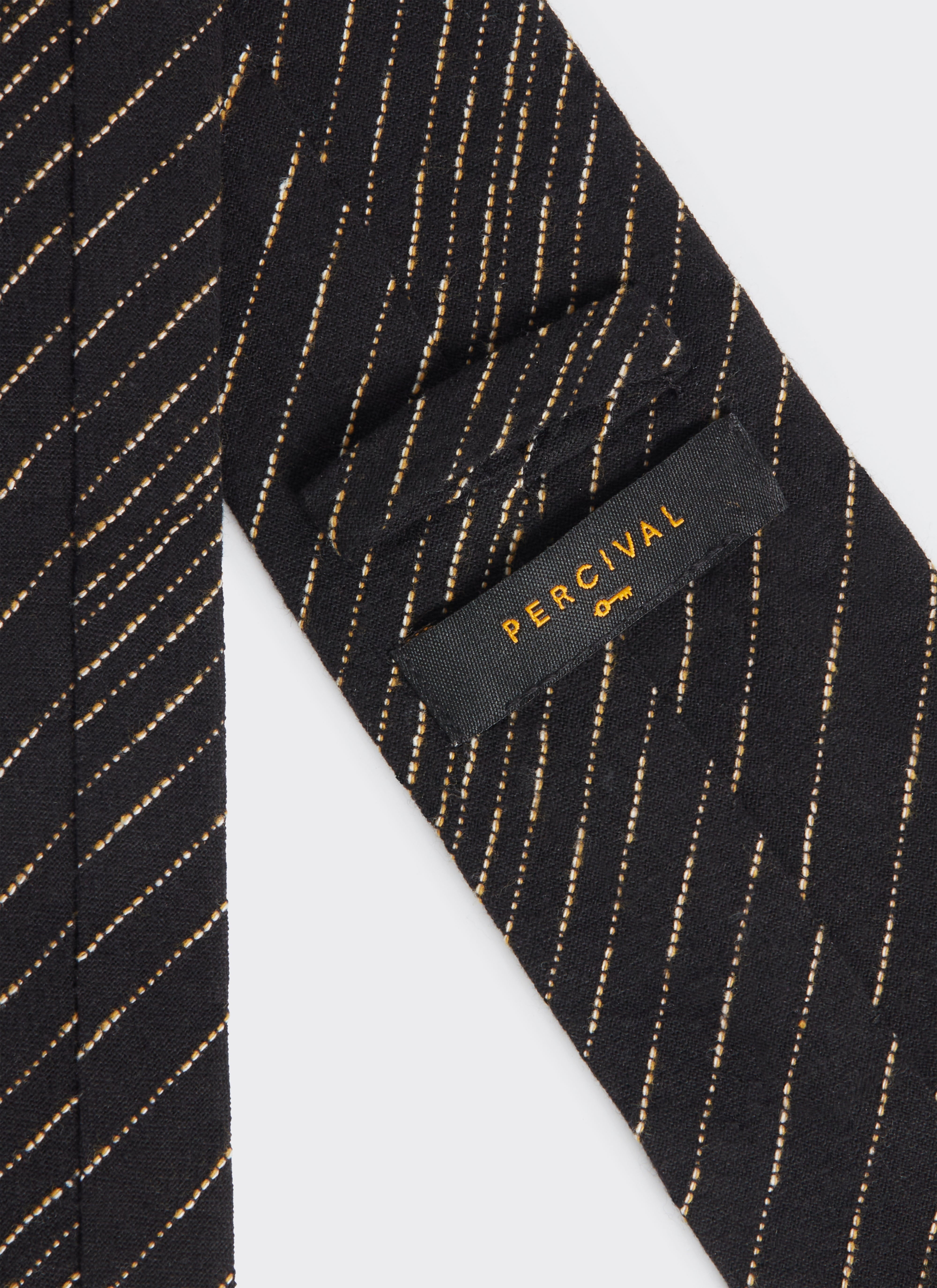 A close-up of the Percival label on the back of the black Leland Tie, showing the white dotted stripe pattern.