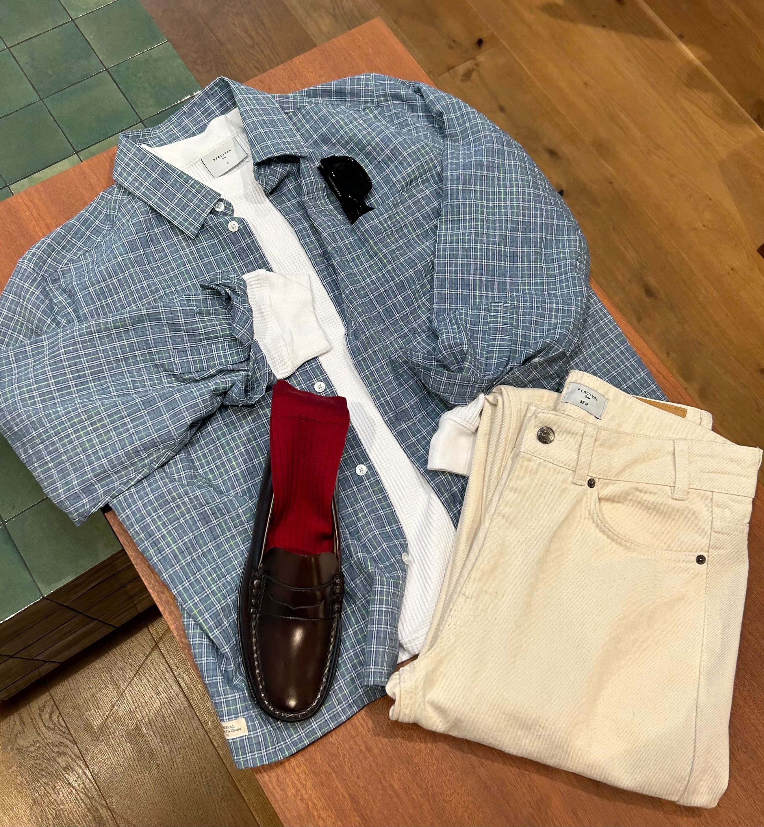 Percival Hinsley Checked Boxy Shirt in blue, styled with a white top, cream trousers, and a brown leather loafer.