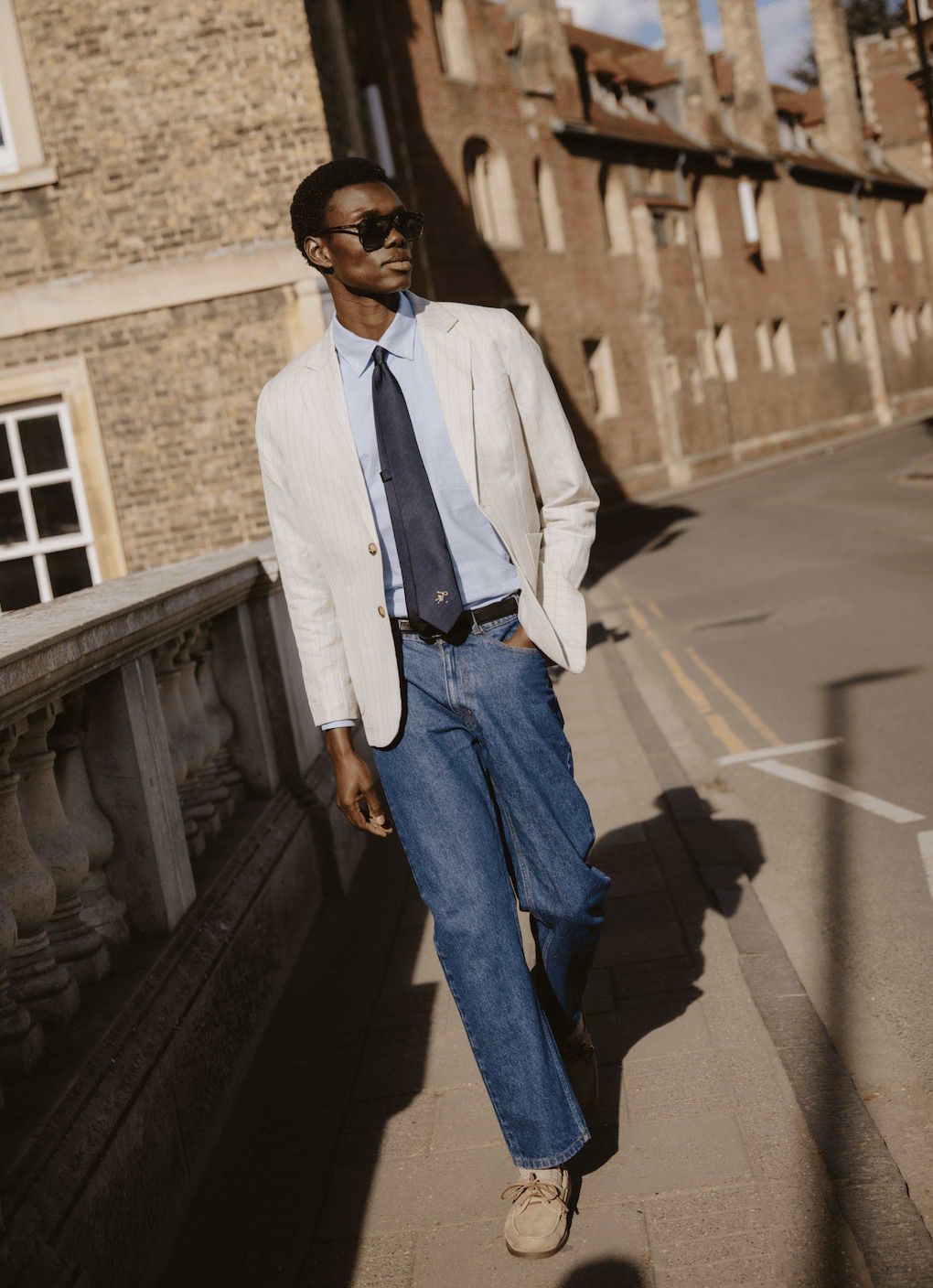 Navy silk World Key Tie by Percival with a gold embroidered motif, styled on a model with a pinstripe blazer.