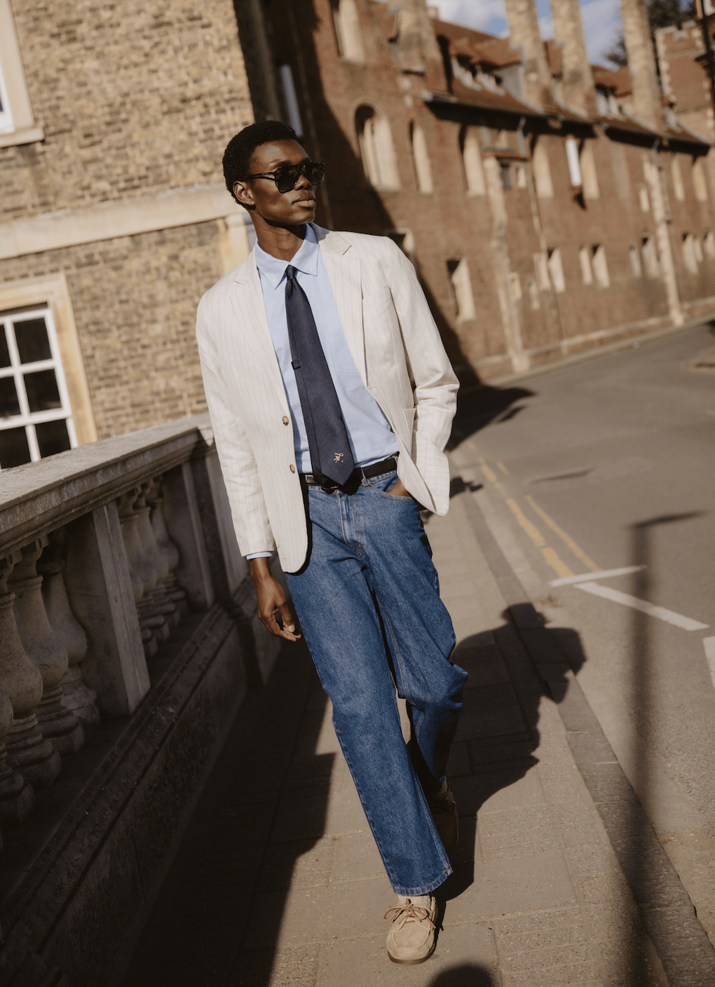 Navy silk World Key Tie by Percival with a gold embroidered motif, styled on a model with a pinstripe blazer.