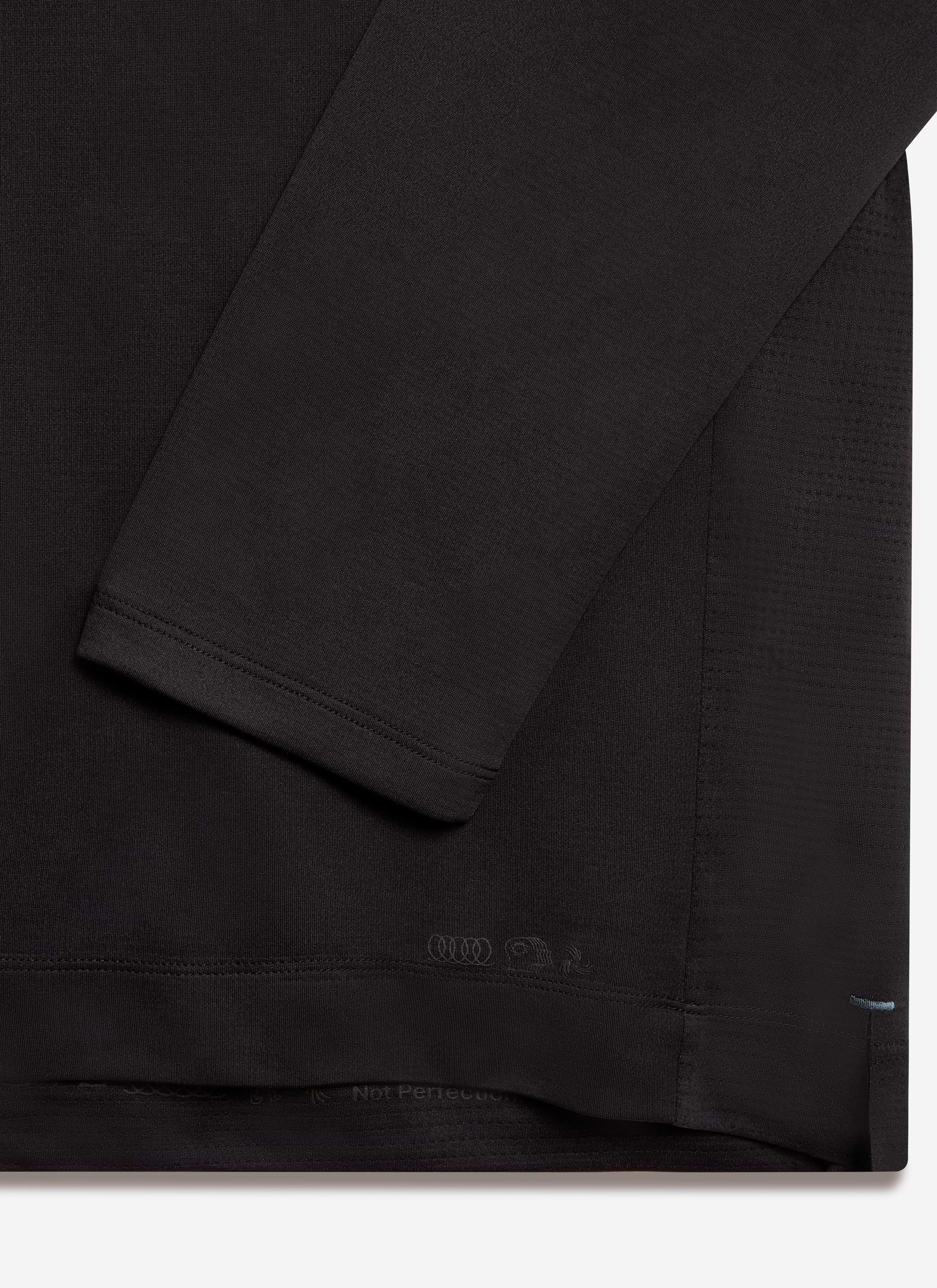 A close-up of the black Percival PCVL Long Sleeve Performance Top, showing the fabric texture and tonal branding at the hem.