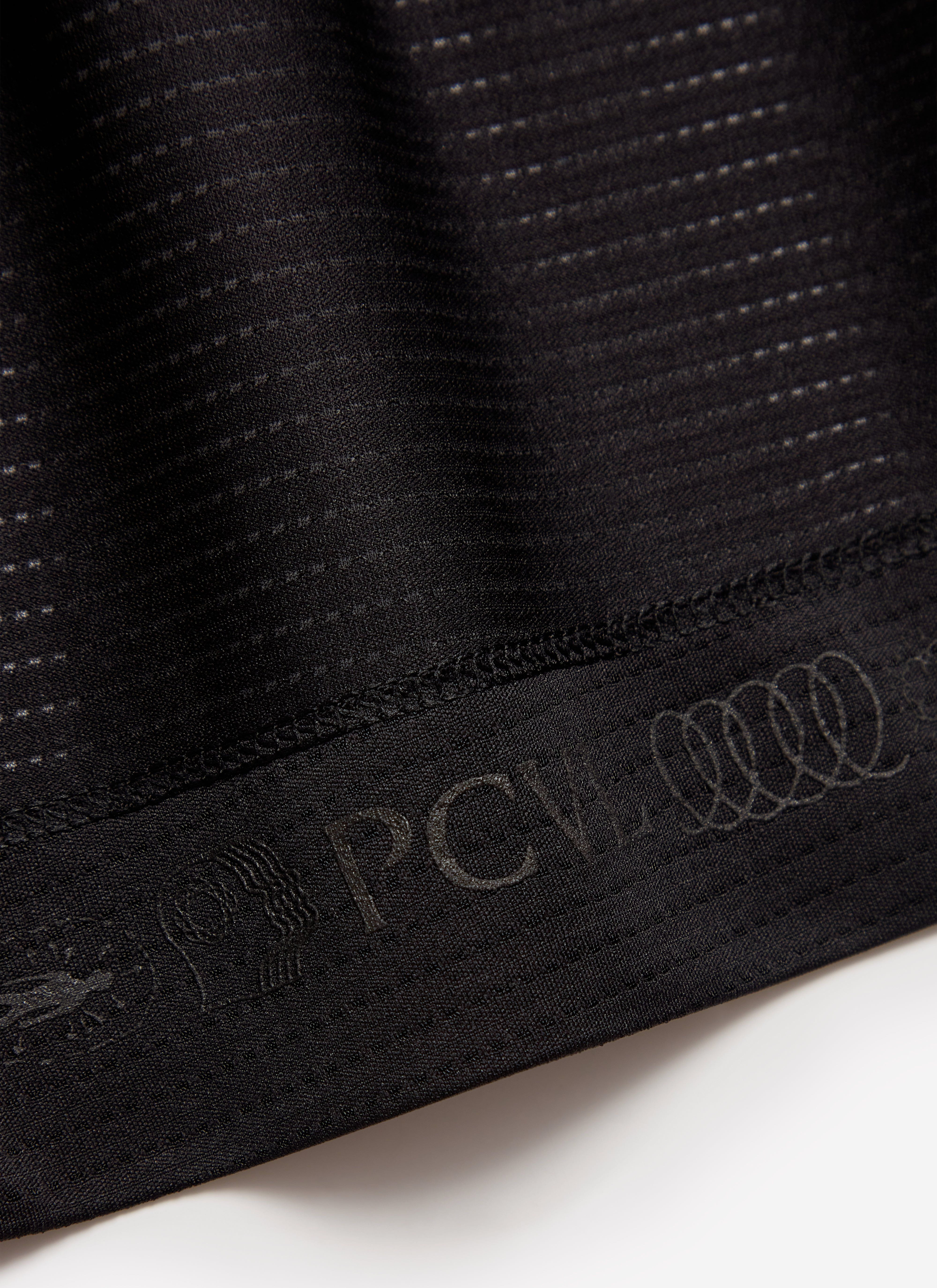 A close-up of the tonal PCVL branding on the hem of the black Percival Performance Top, showing the technical fabric.