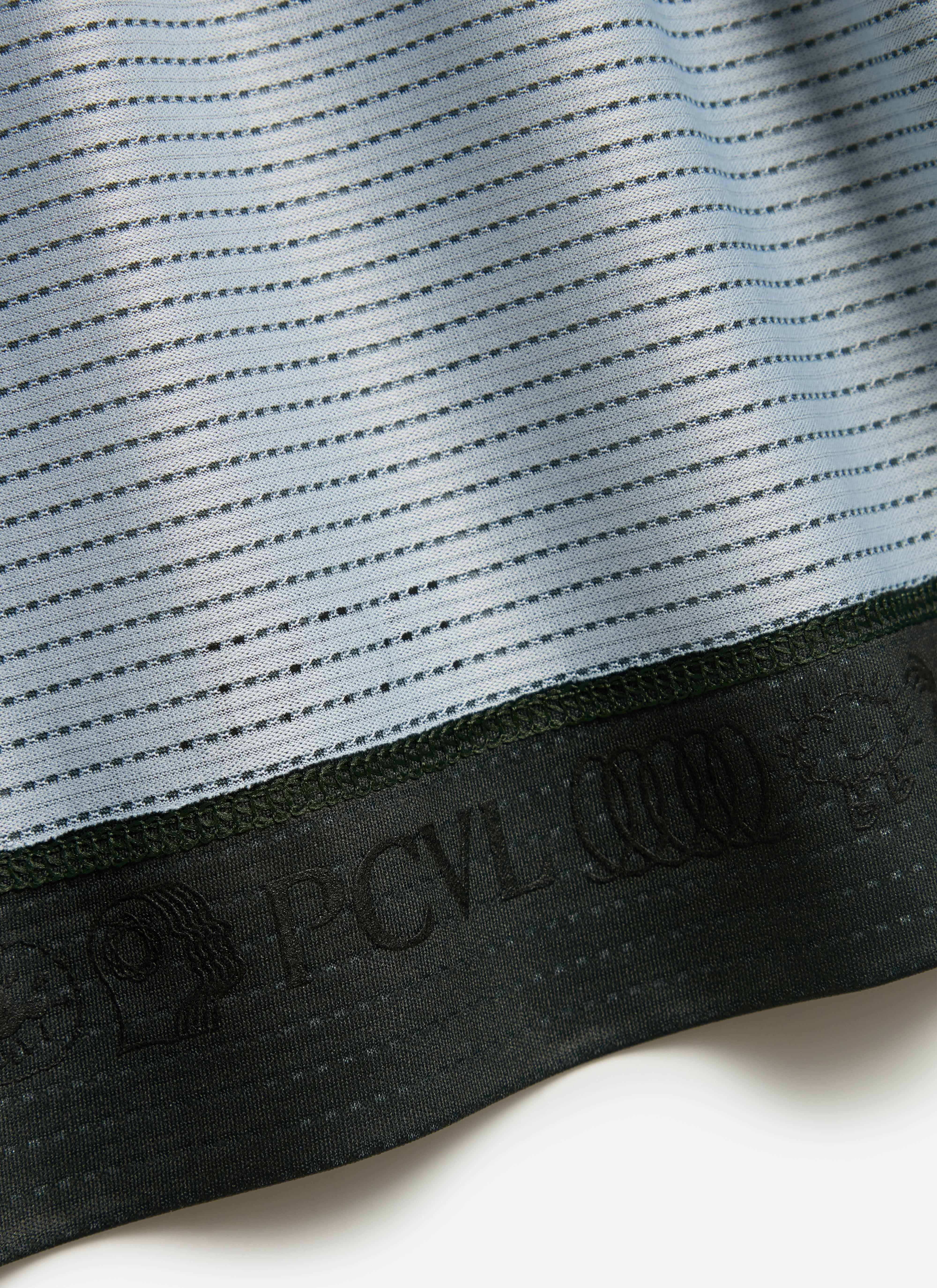 A close-up of the Percival PCVL Performance Top in Forest, detailing the ventilated fabric and the embossed logo on the hem.