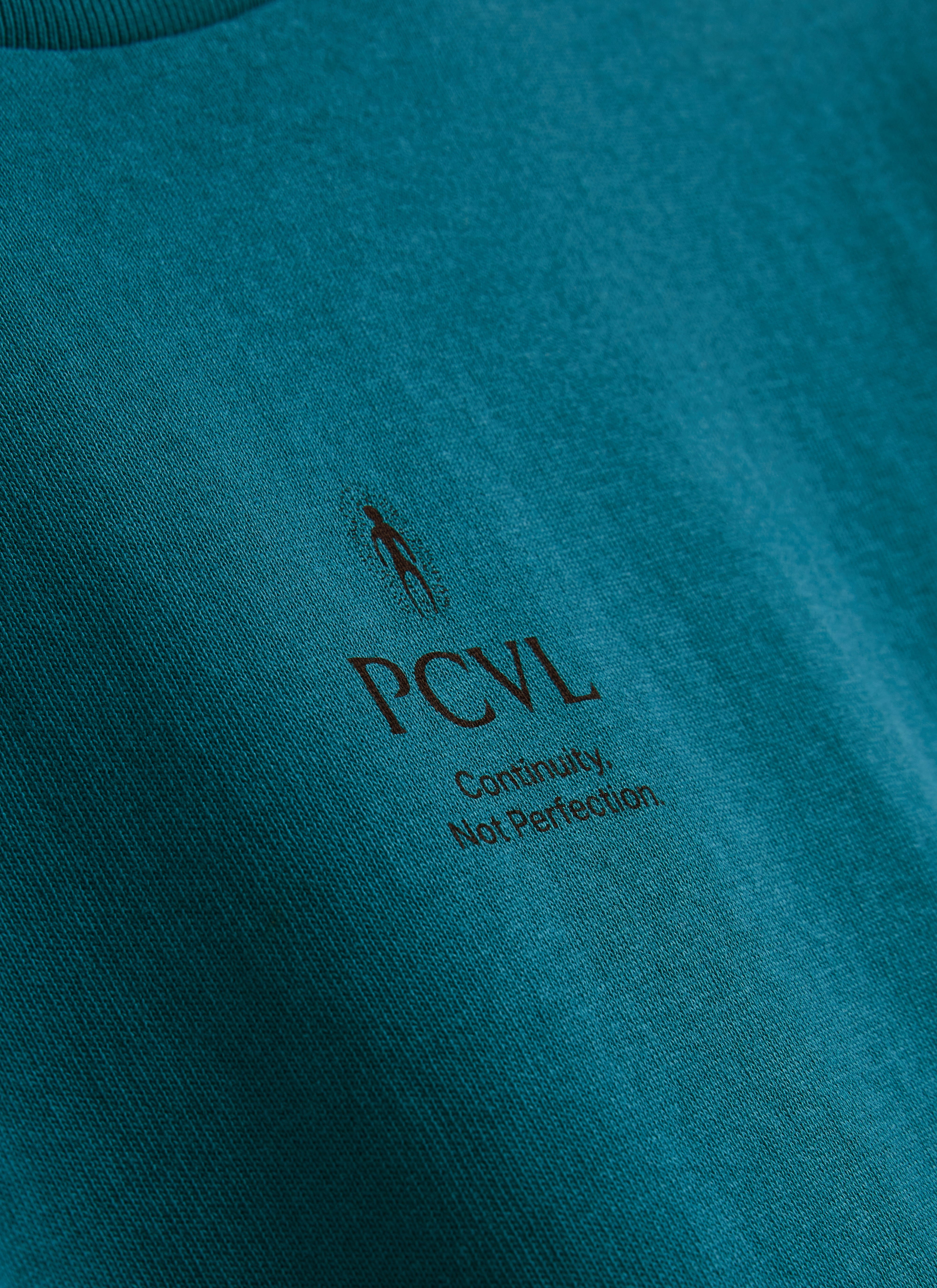 A close-up of the 'Continuity, Not Perfection' PCVL chest print on the blue Aura Boxy T-shirt by Percival.