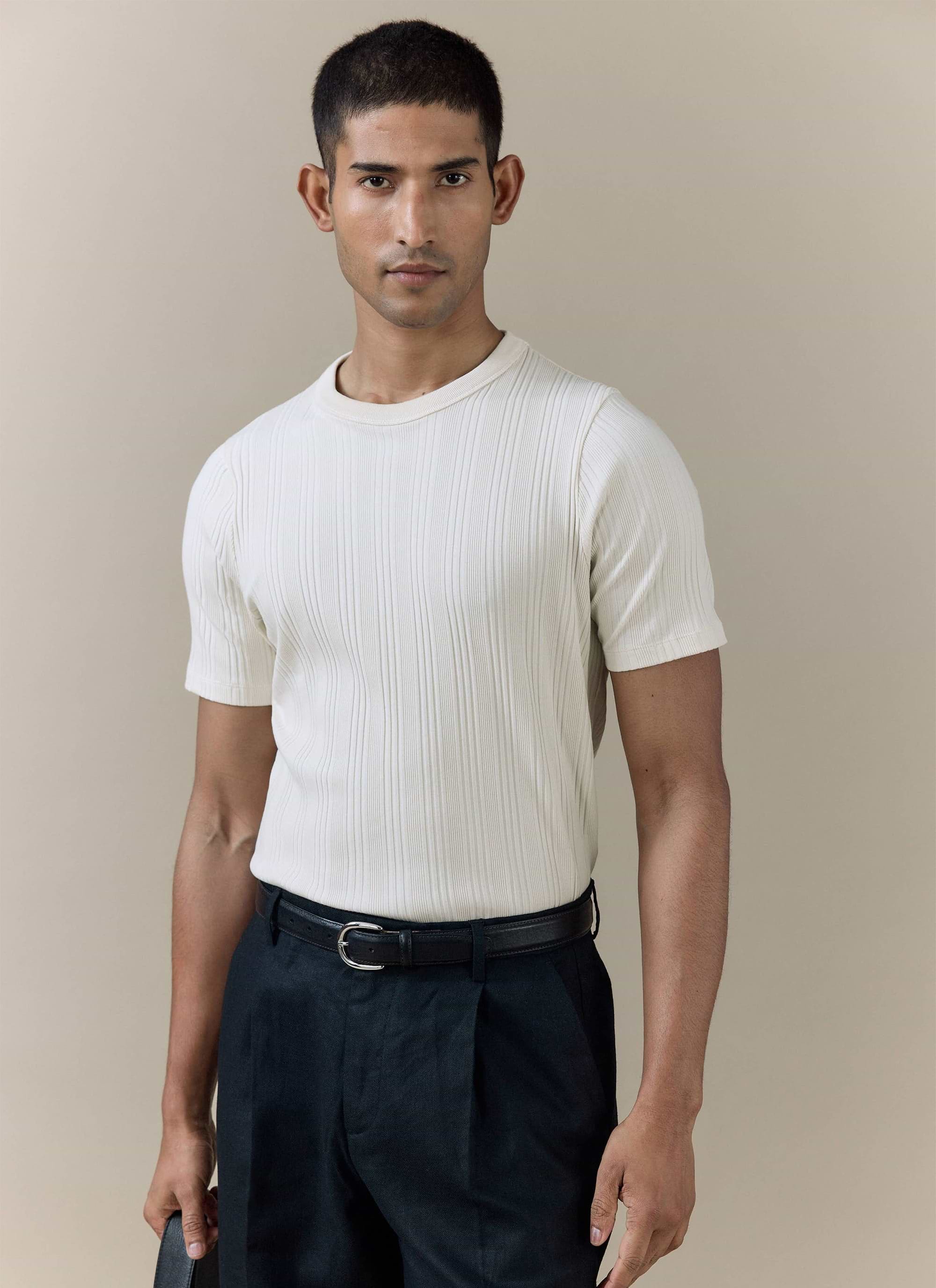 A model wearing the cream Percival Leon Ribbed T Shirt in organic cotton, featuring a textured vertical rib design.