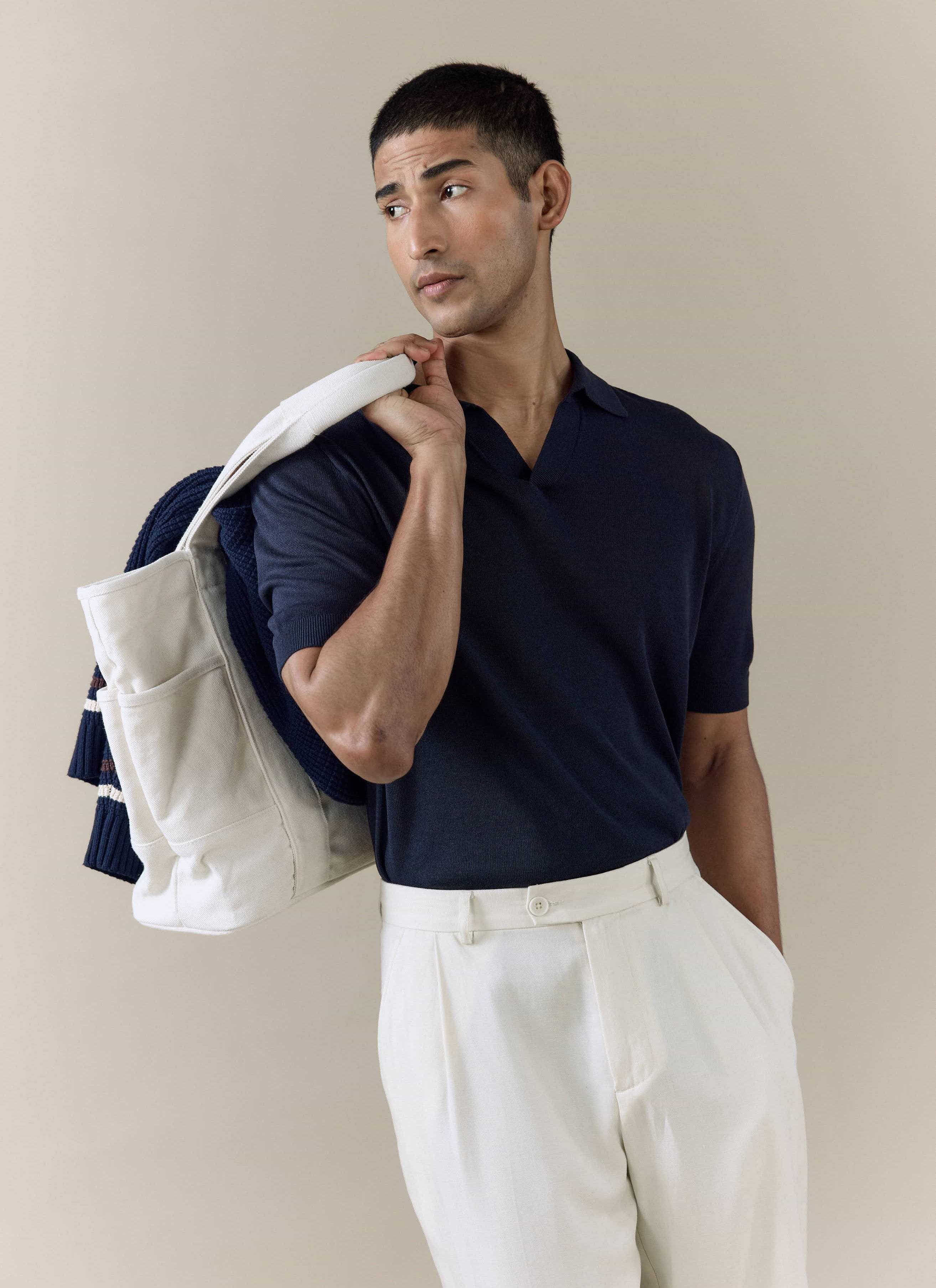 Model wearing the navy Percival Laurence Knitted Polo in a linen-lyocell blend, paired with cream pleated trousers.
