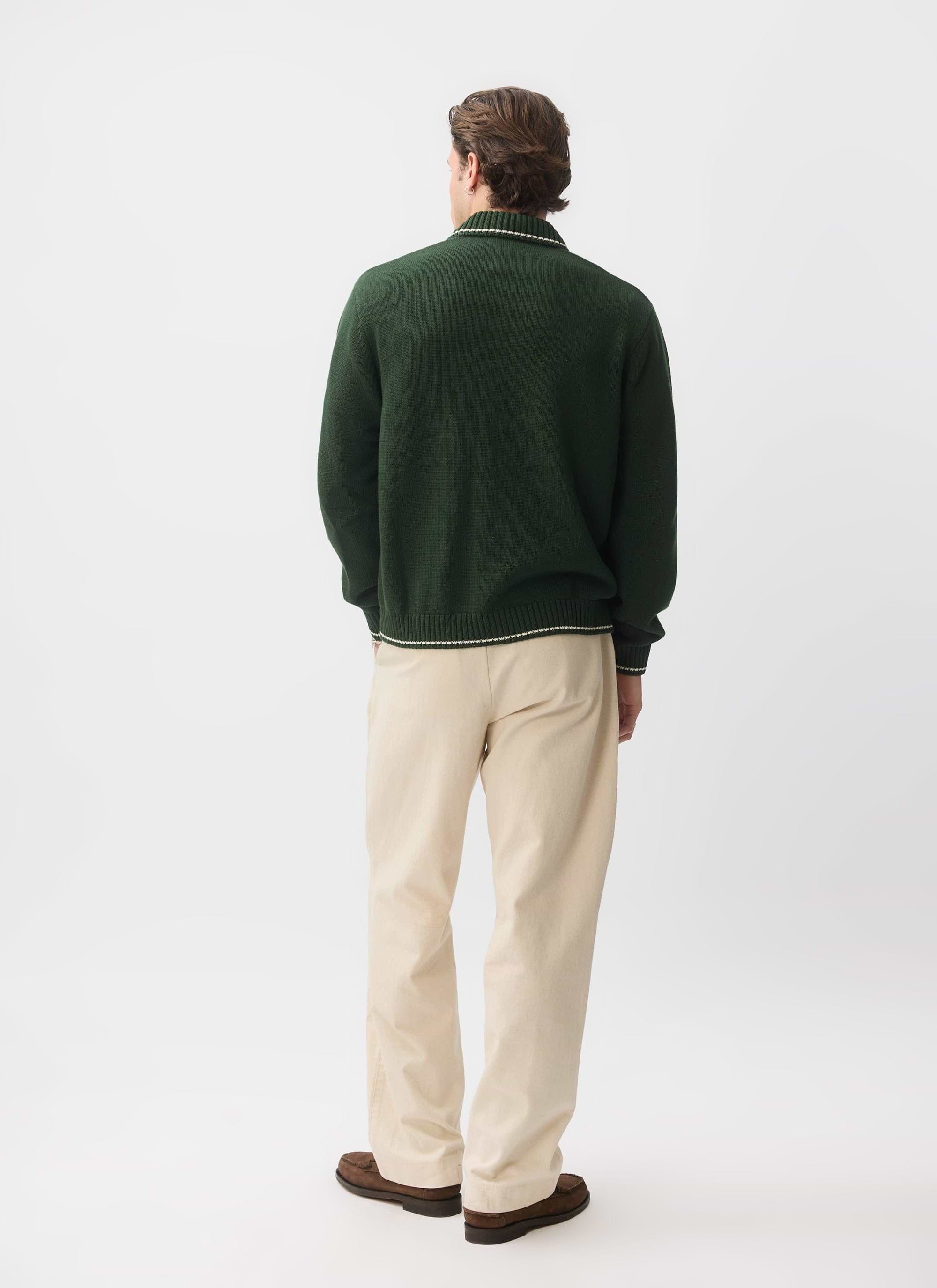 Back view of a model in the Percival Gardner Dense Knitted Zip Cardigan in forest green, styled with cream trousers.