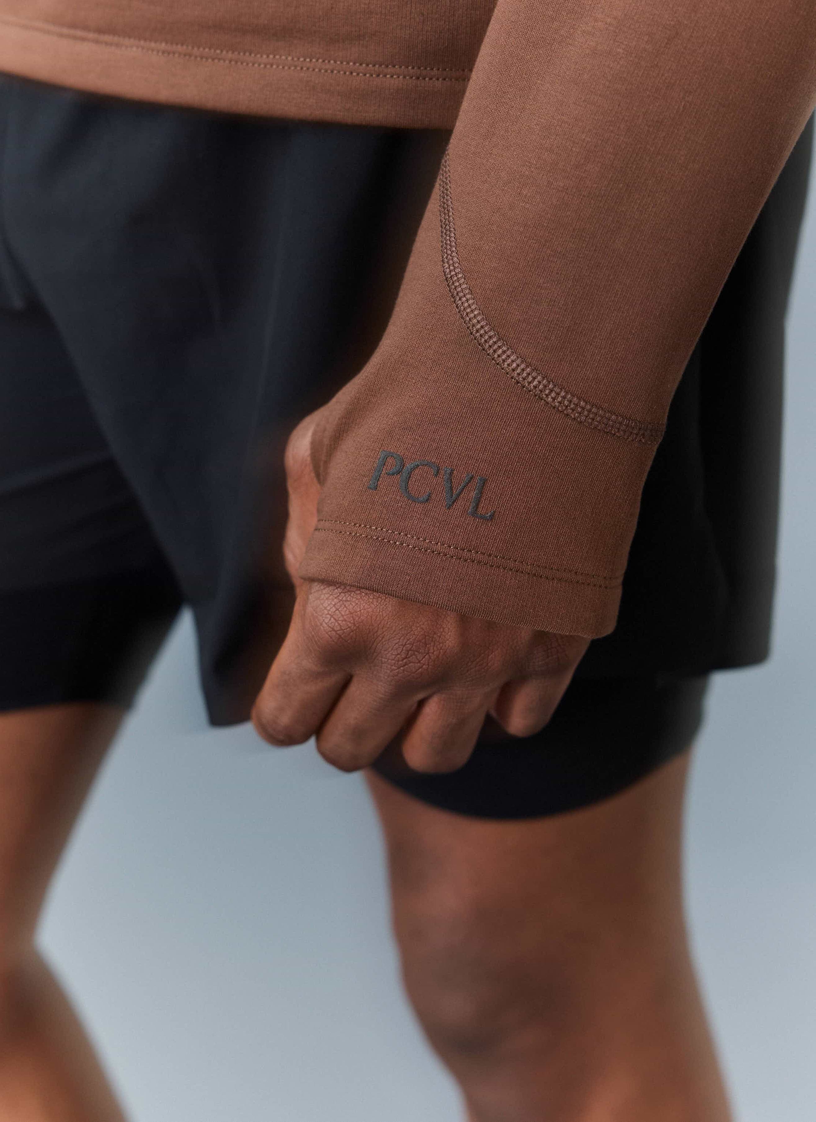 A close-up of the Percival PCVL Base Layer Quarter Zip in rust, showing the thumb loop and tonal PCVL logo on the cuff.