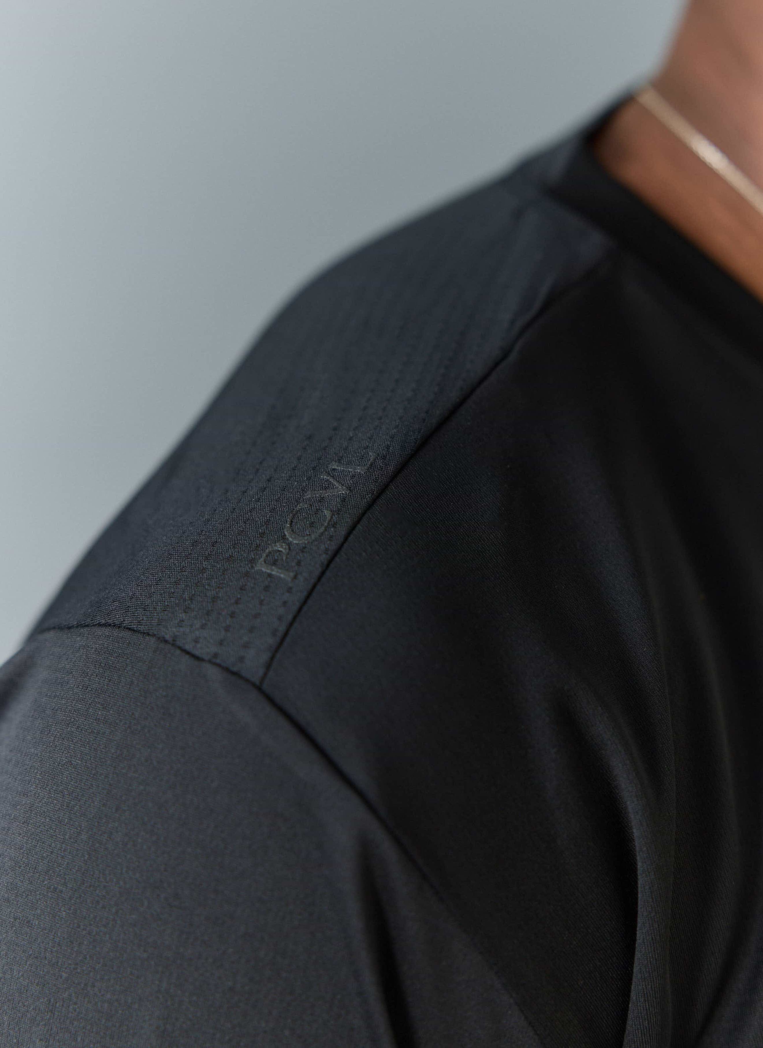 A close-up of the tonal 'PCVL' branding on the shoulder of the black Long Sleeve Printed Performance Top by Percival.
