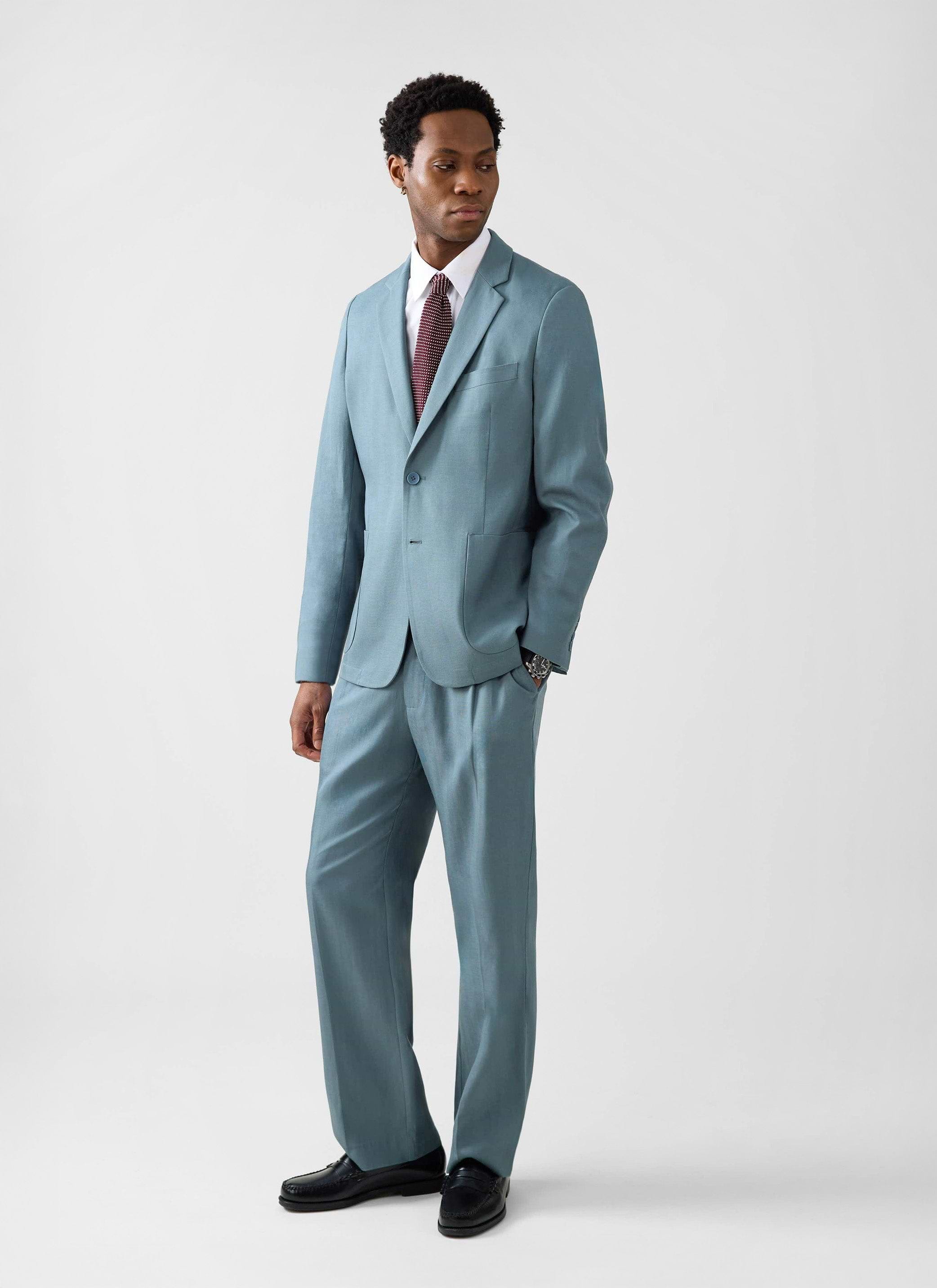 A man models the Percival Lyocell Regular Blazer in Slate Blue with matching trousers against a studio background.