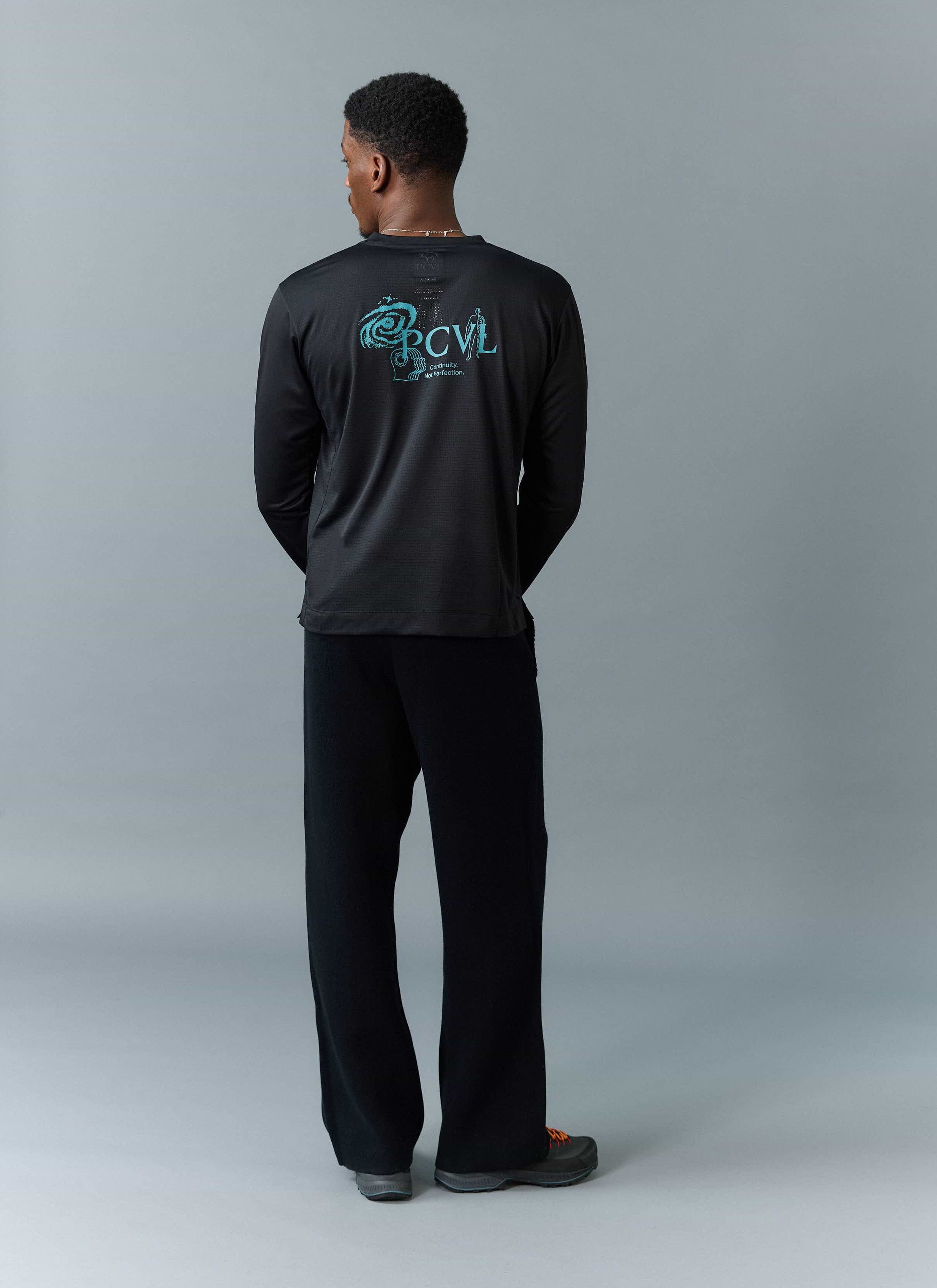 Back view of a model wearing the PCVL Long Sleeve Printed Performance Top in black by Percival, showing the blue graphic.