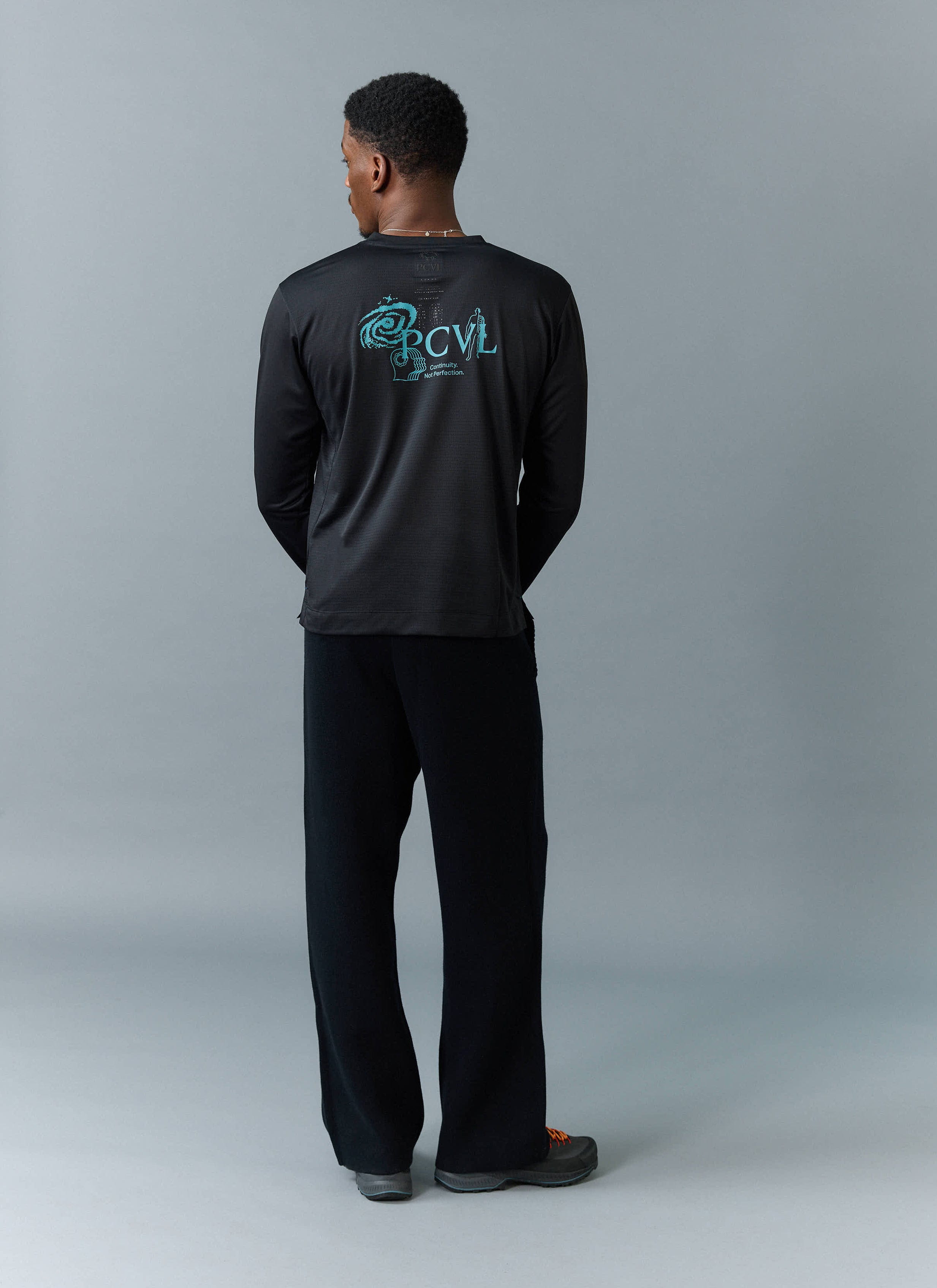 Back view of a model wearing the PCVL Long Sleeve Printed Performance Top in black by Percival, showing the blue graphic.
