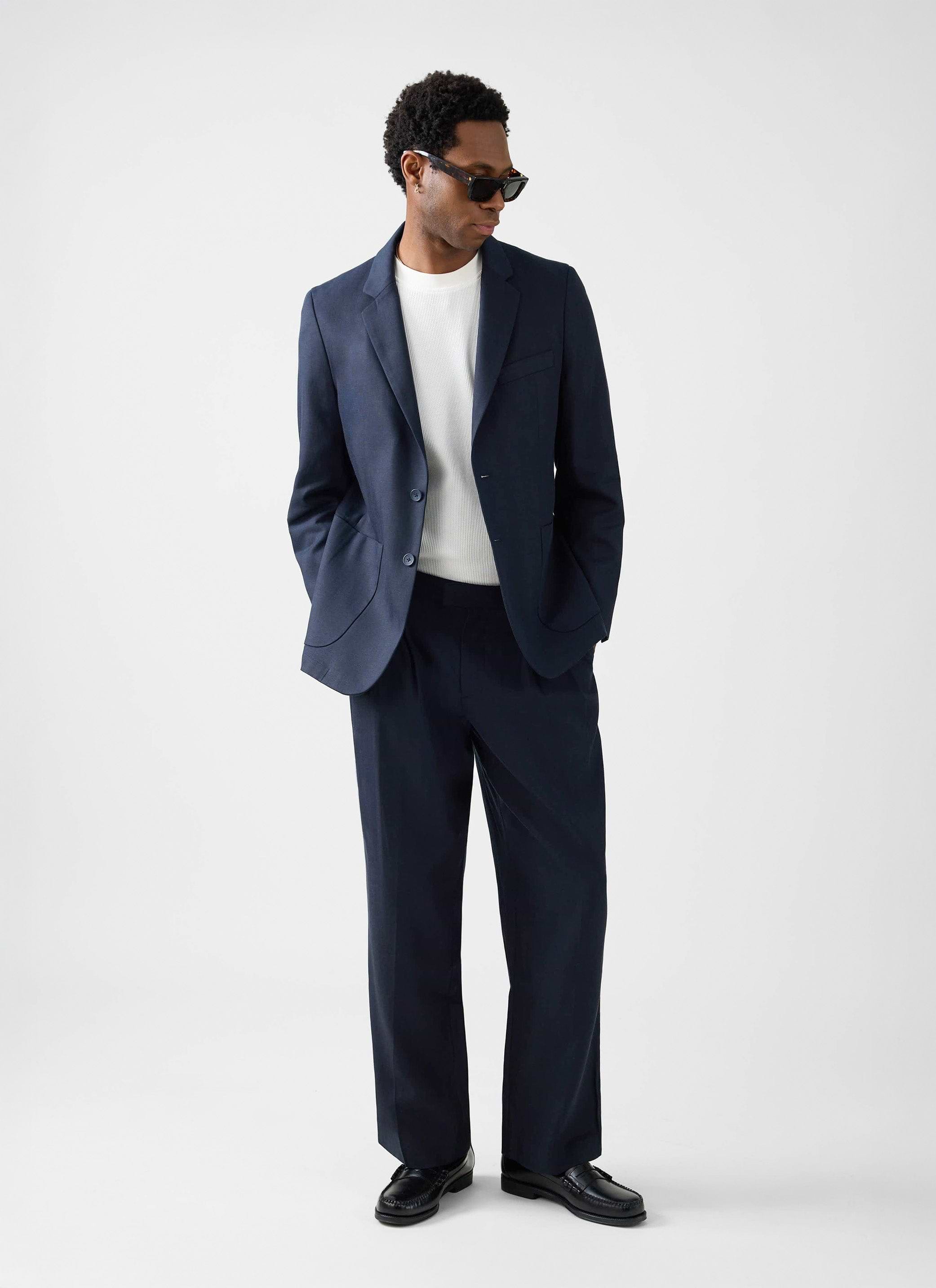 A model wears the Percival Lyocell Regular Blazer and Trousers in navy, styled with a white t-shirt and sunglasses.