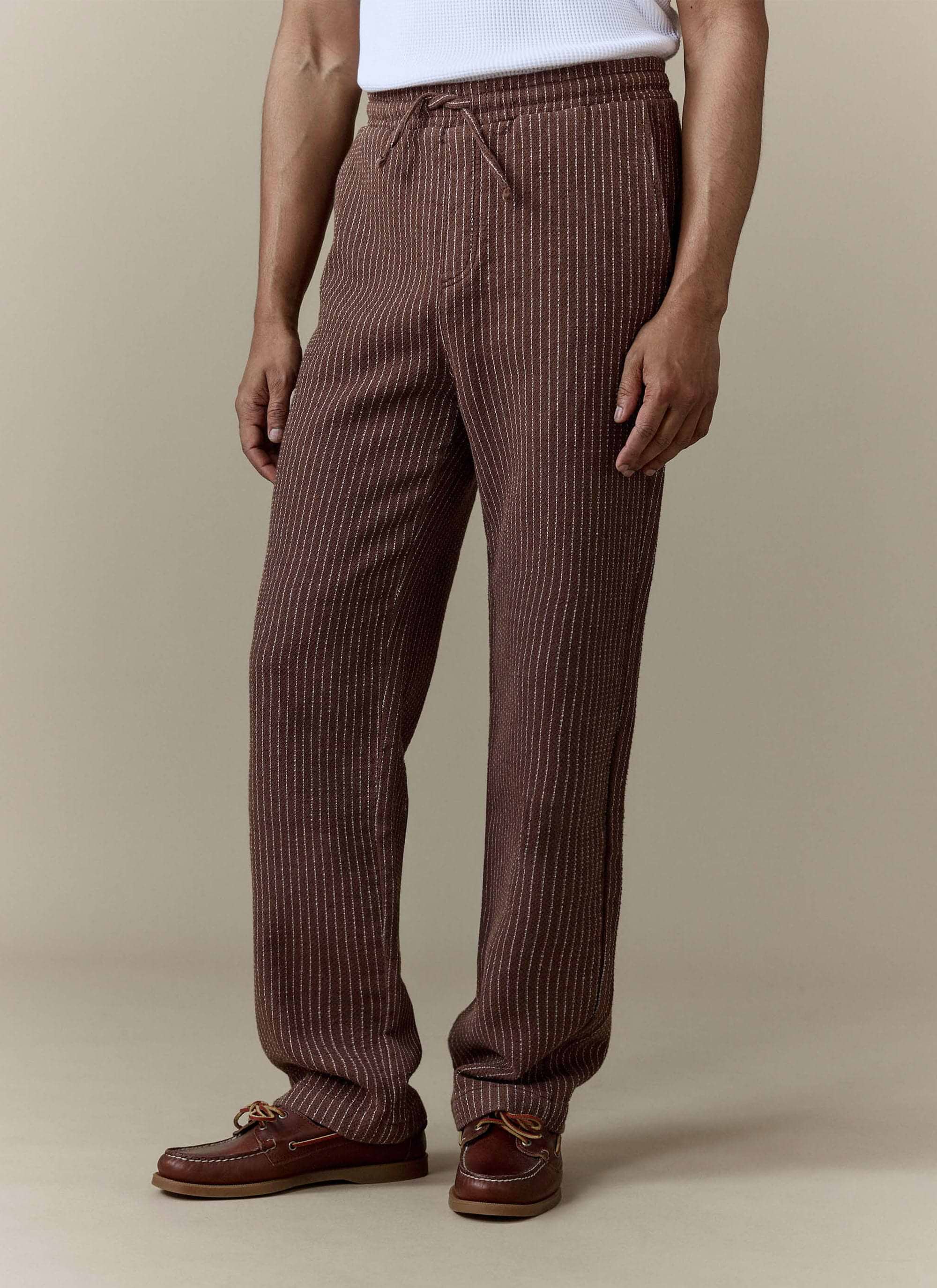A model wears the brown linen Sorrento Wide Leg Trousers from Percival, styled with a white top and brown boat shoes.
