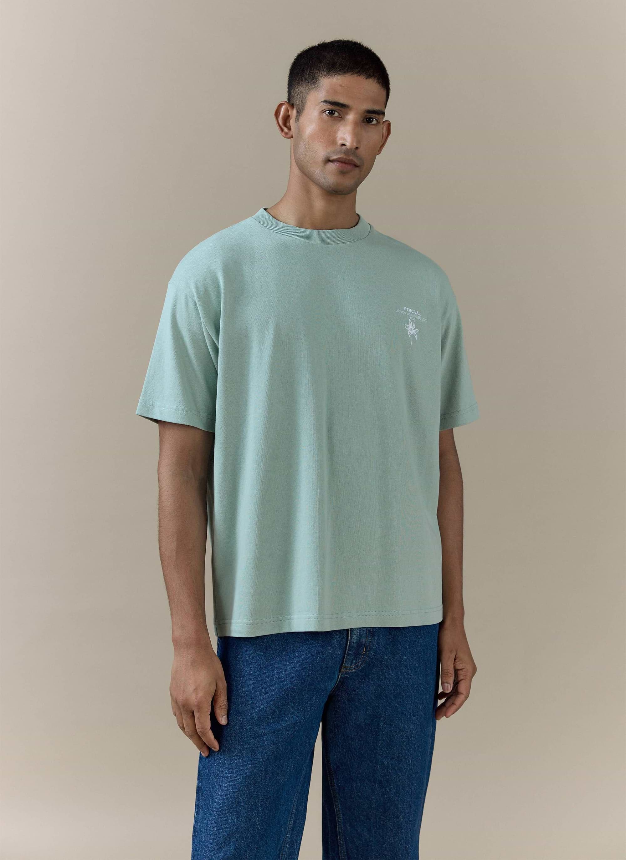 Percival's sage green Melvin Oversized T Shirt in organic cotton, featuring a small chest graphic and relaxed fit.