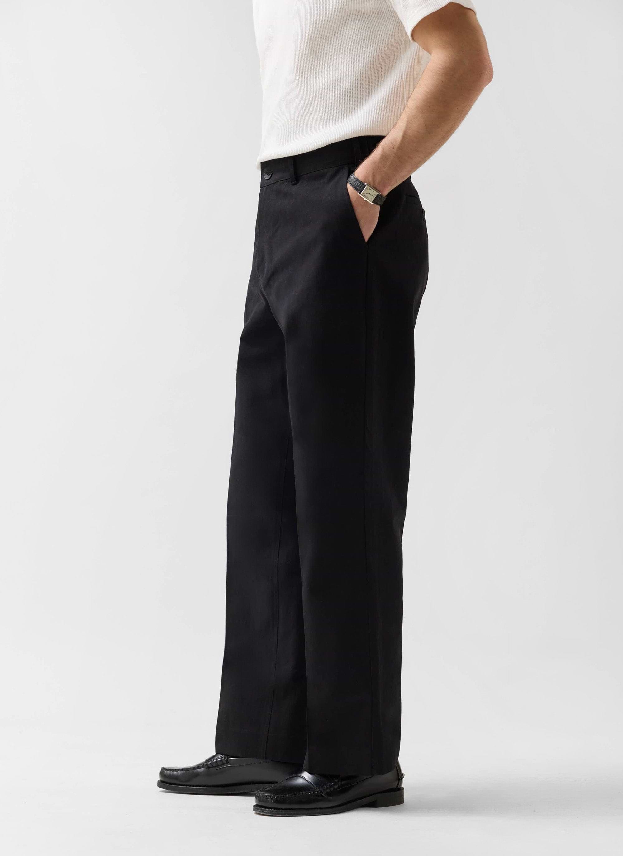 Side view of a model wearing the Percival Wide Leg Chino in black, paired with a white ribbed top and black loafers.