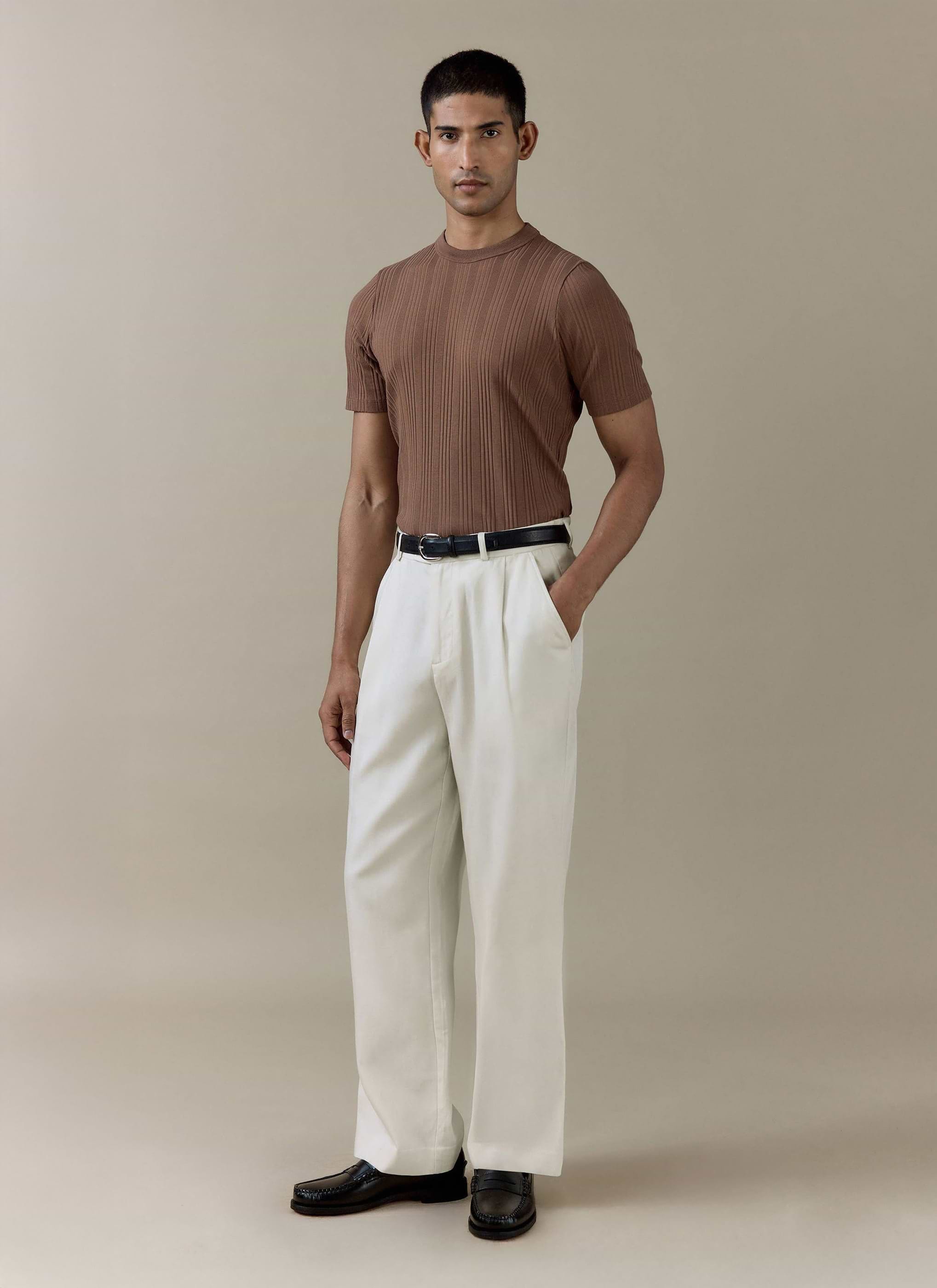 Male model wears the Percival Leon Ribbed T Shirt in brown cotton, styled with off-white trousers and black loafers.