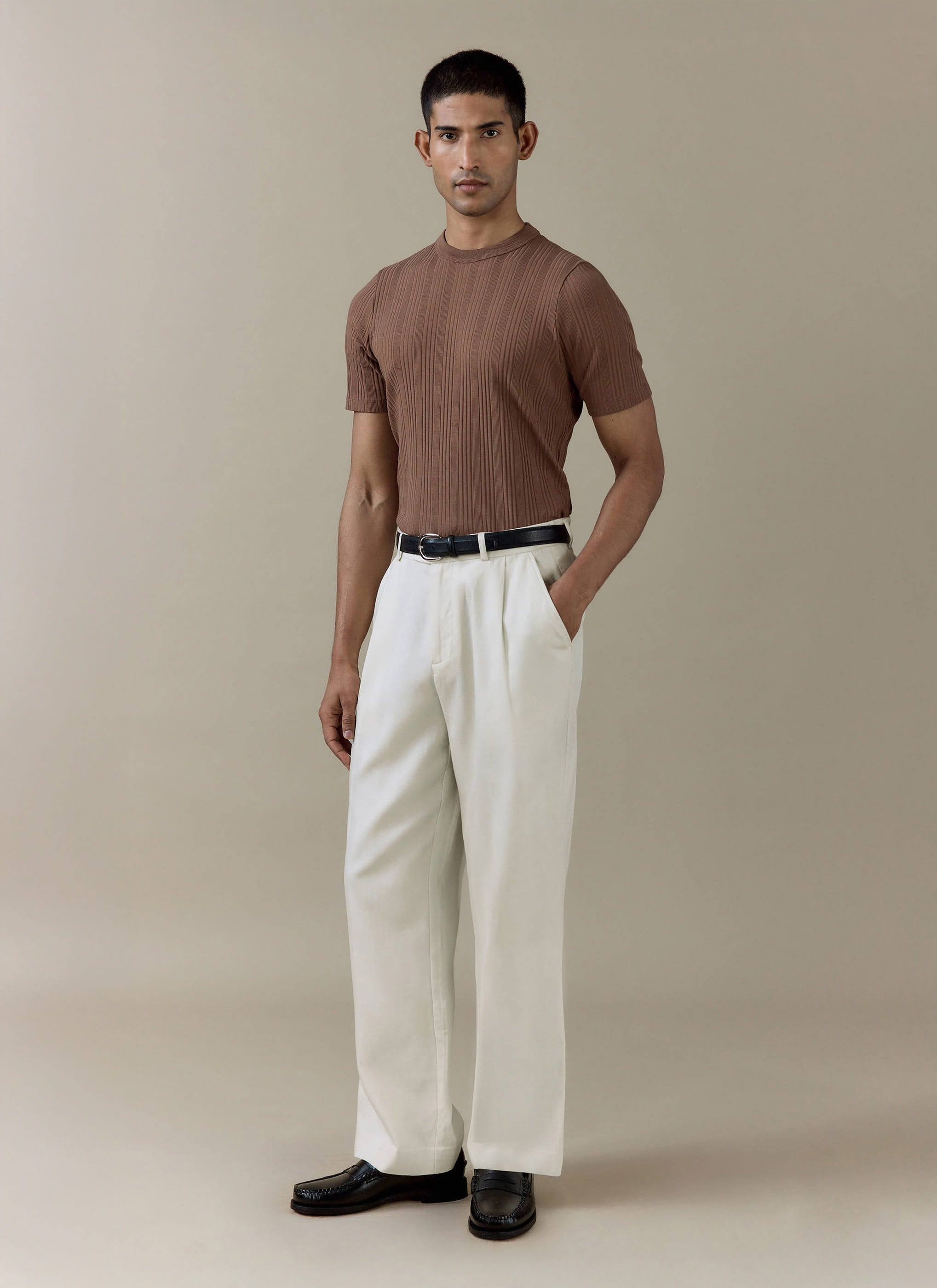 Male model wears the Percival Leon Ribbed T Shirt in brown cotton, styled with off-white trousers and black loafers.
