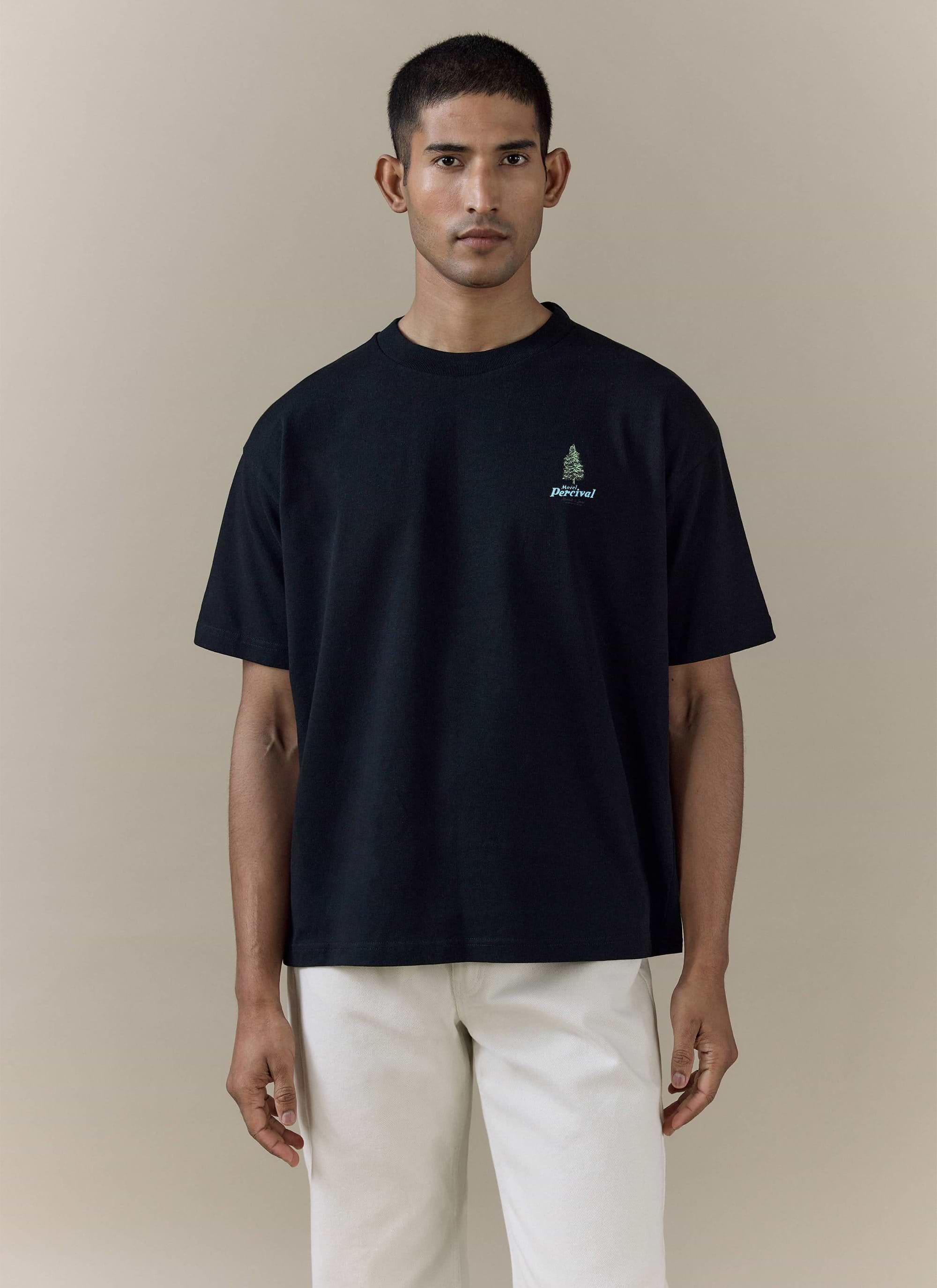 Percival Arnold Oversized T Shirt in black organic cotton with a green tree chest embroidery, worn by a male model.