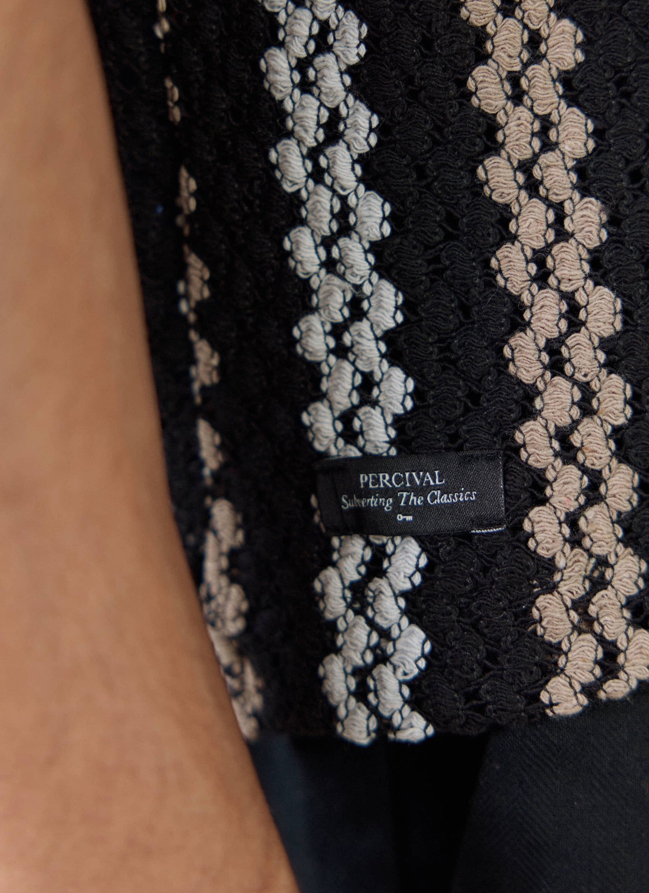 A close-up of the textured crochet stripes and brand label on the Percival Wade Crochet Boxy Shirt in black.