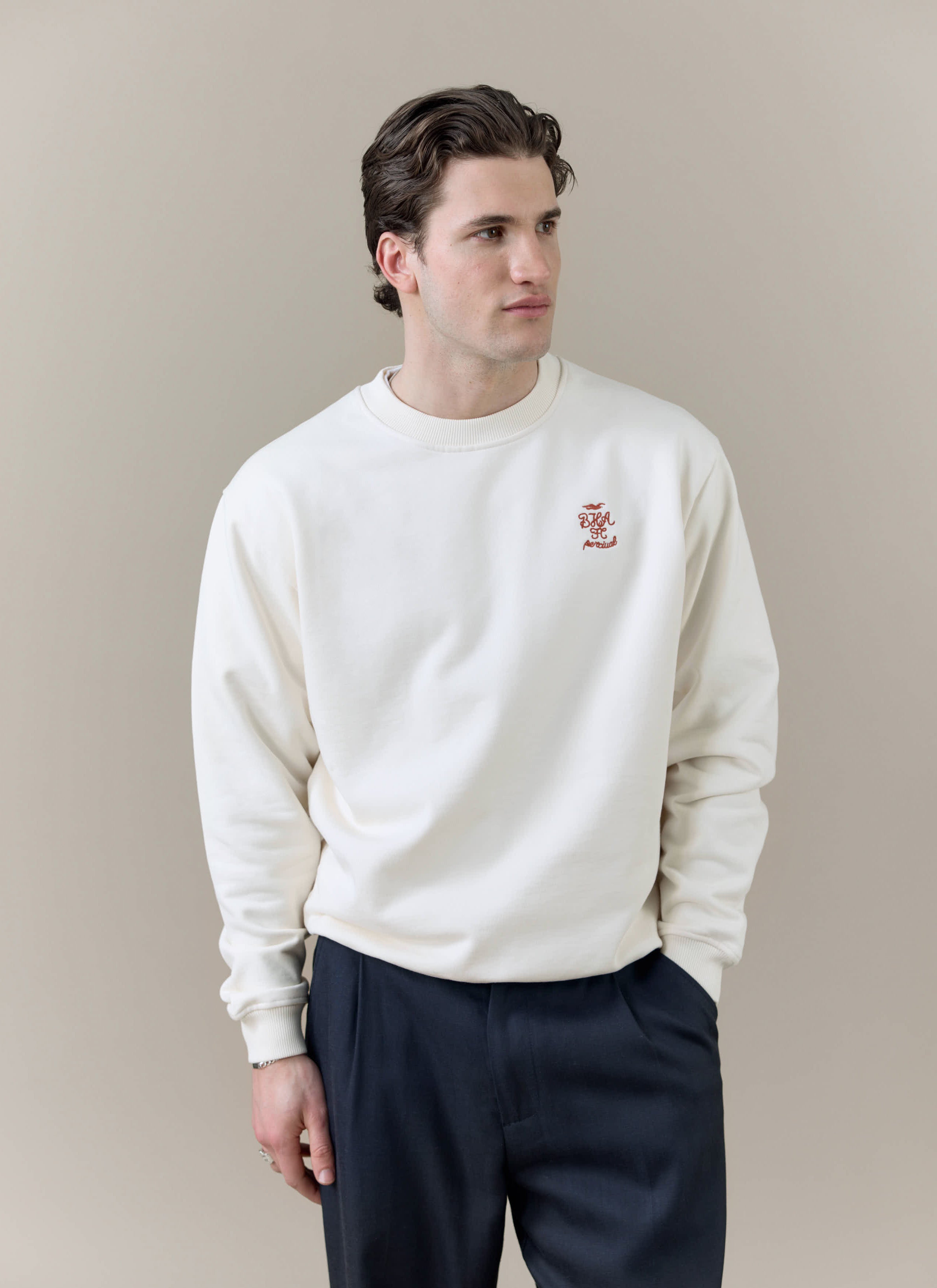 A model wears the Percival x Brighton & Hove Albion F.C. collaboration sweatshirt in cream with navy trousers.