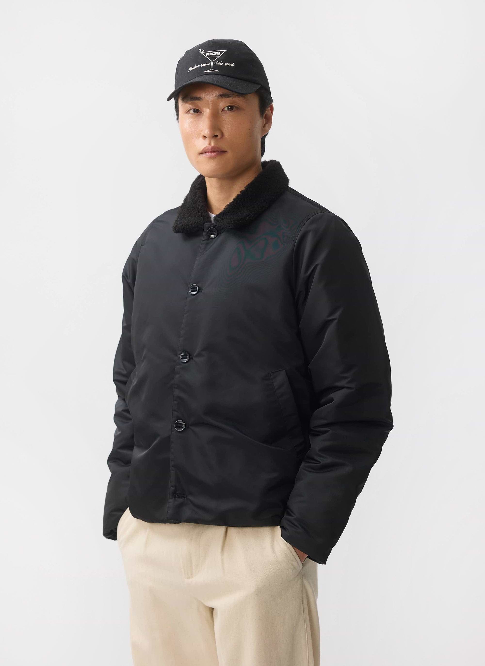 A man models the black Percival Doppio Bomber Jacket with its shearling collar against a white studio background.