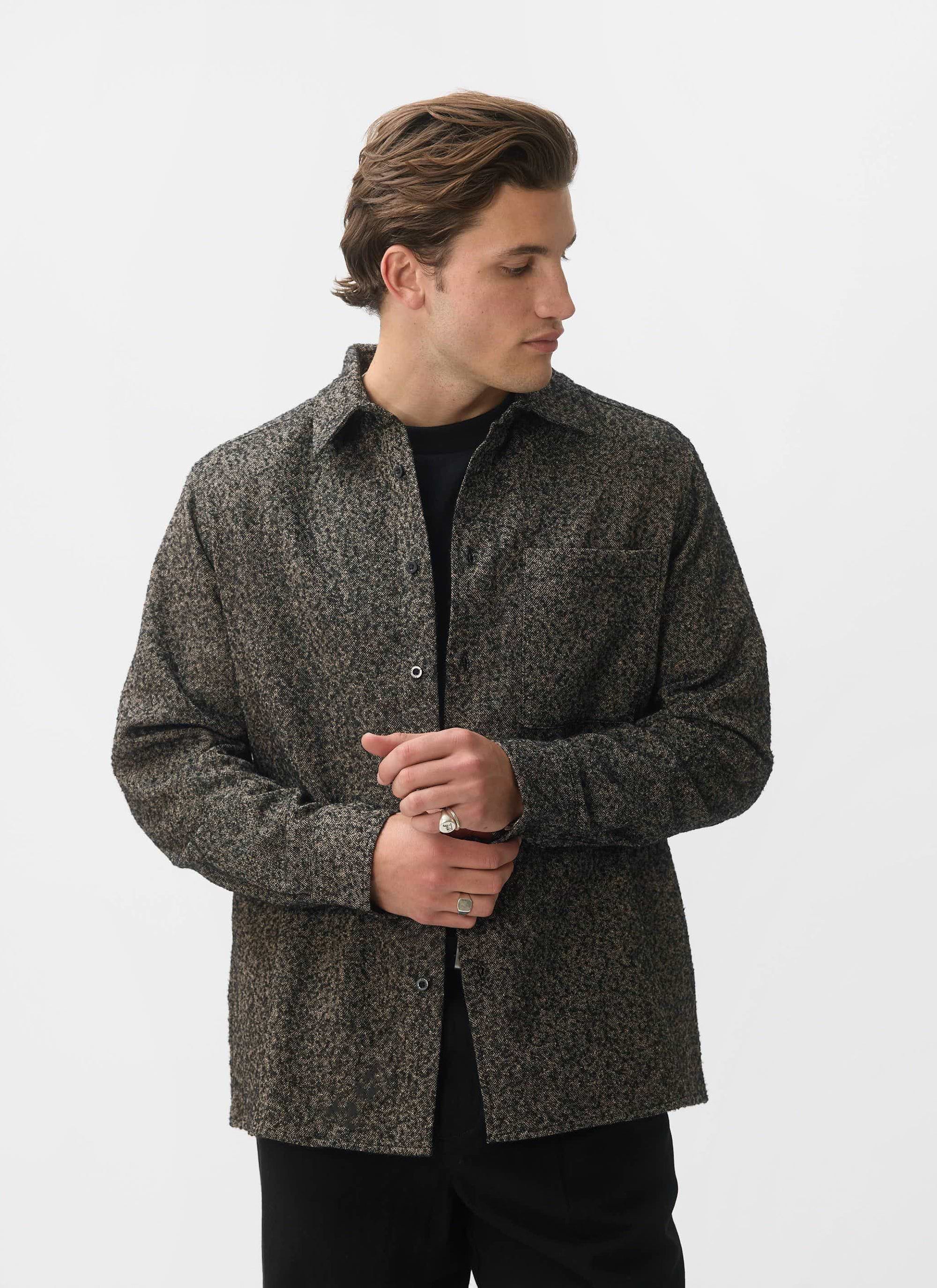 A man models the Percival Blyton Long Sleeve Shirt in nep grey, adjusting his cuff against a white background.