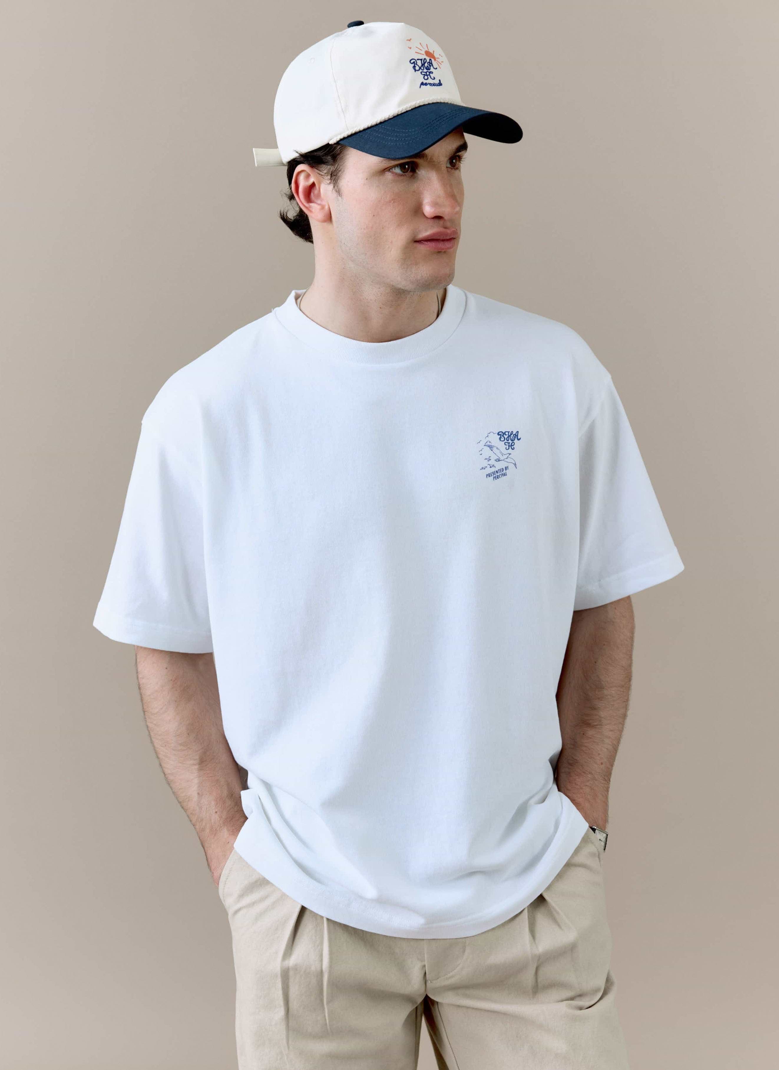 A model wears the white Beach Front T Shirt from the Percival x Brighton & Hove Albion F.C. collaboration, styled with a cap.