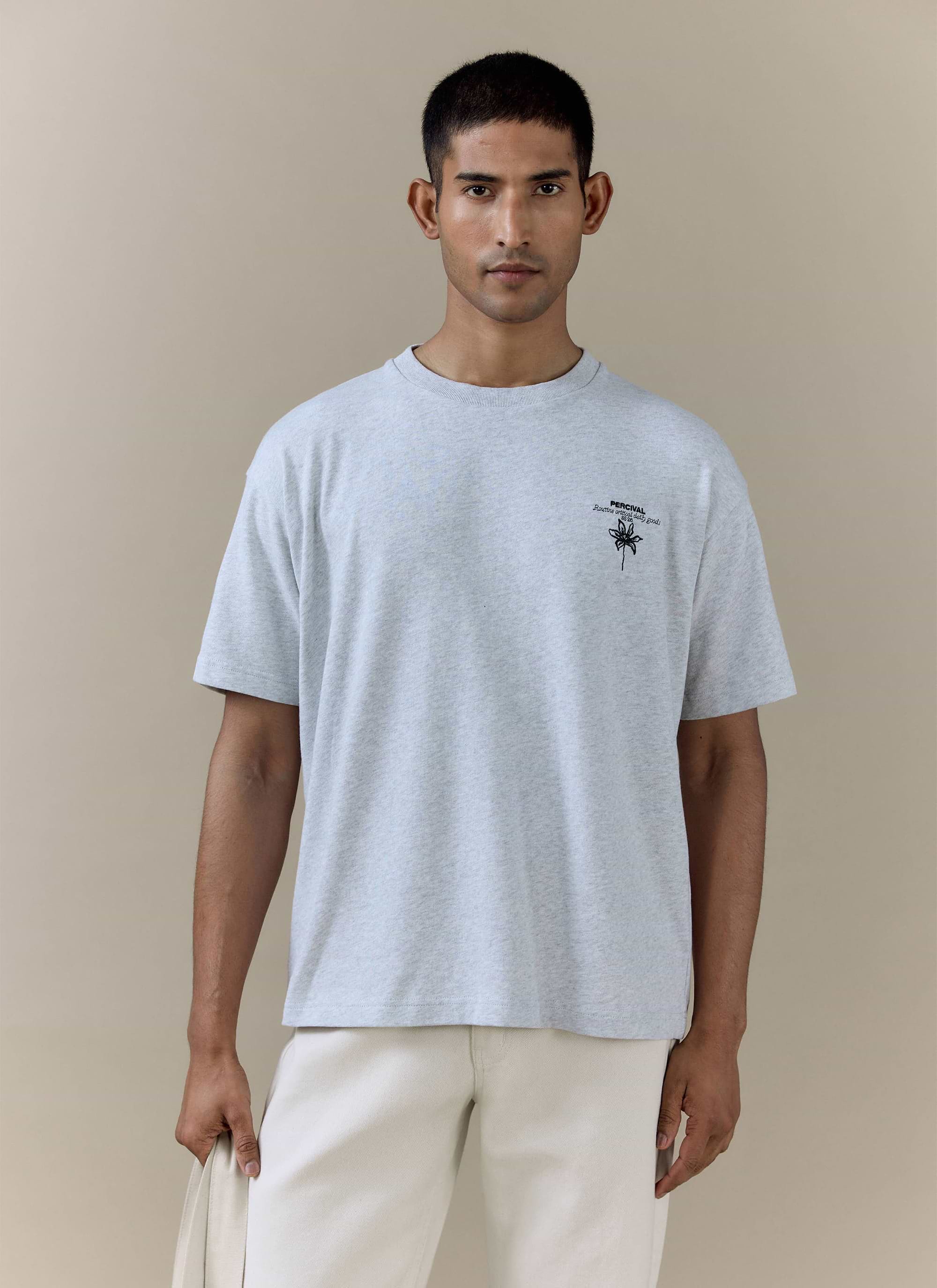 A model wearing the Percival Melvin Oversized T Shirt in grey organic cotton, featuring a black floral chest graphic.