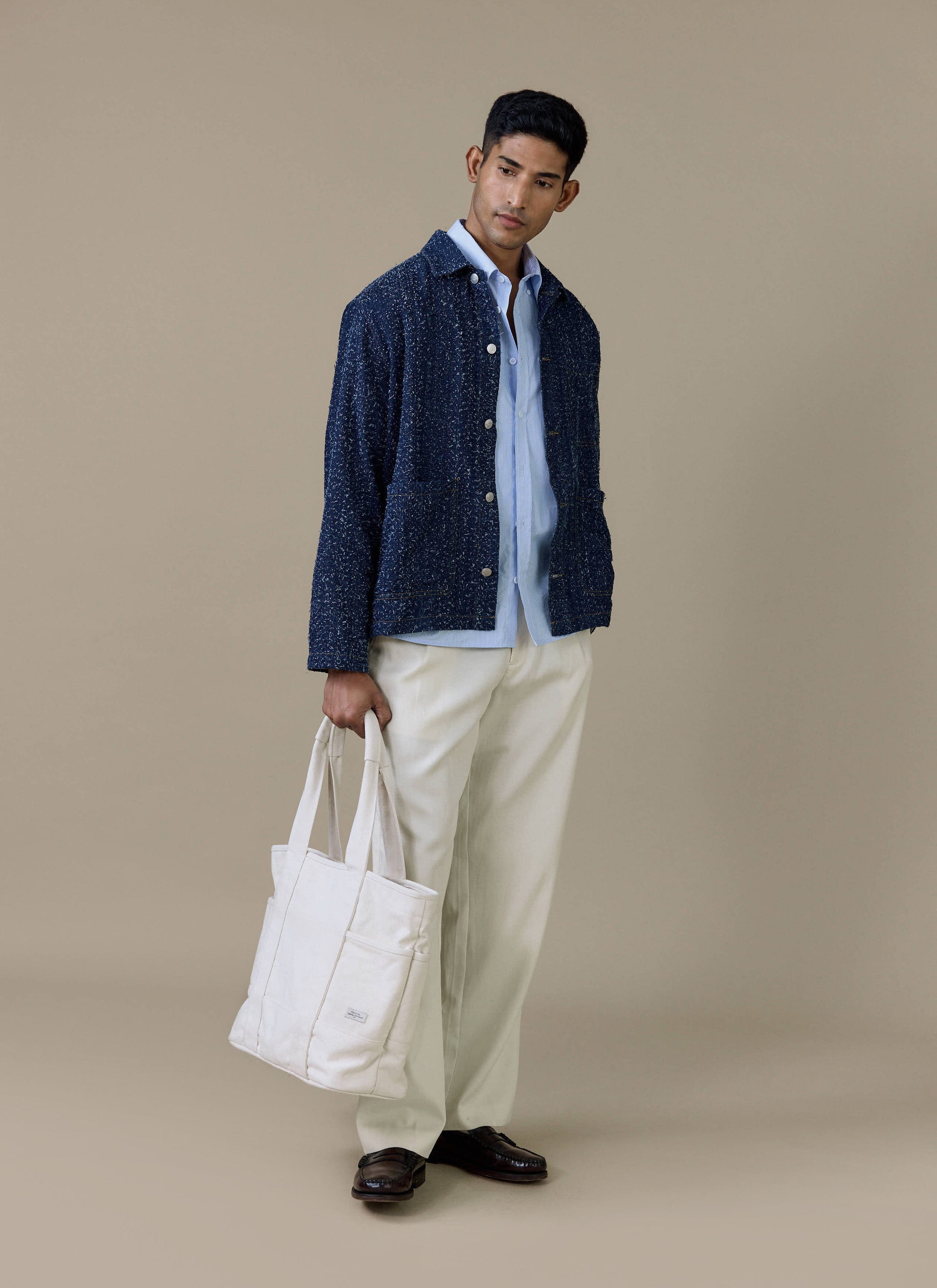A model wearing the navy Parsons Chore Jacket from Percival, styled with cream trousers and a matching tote bag.