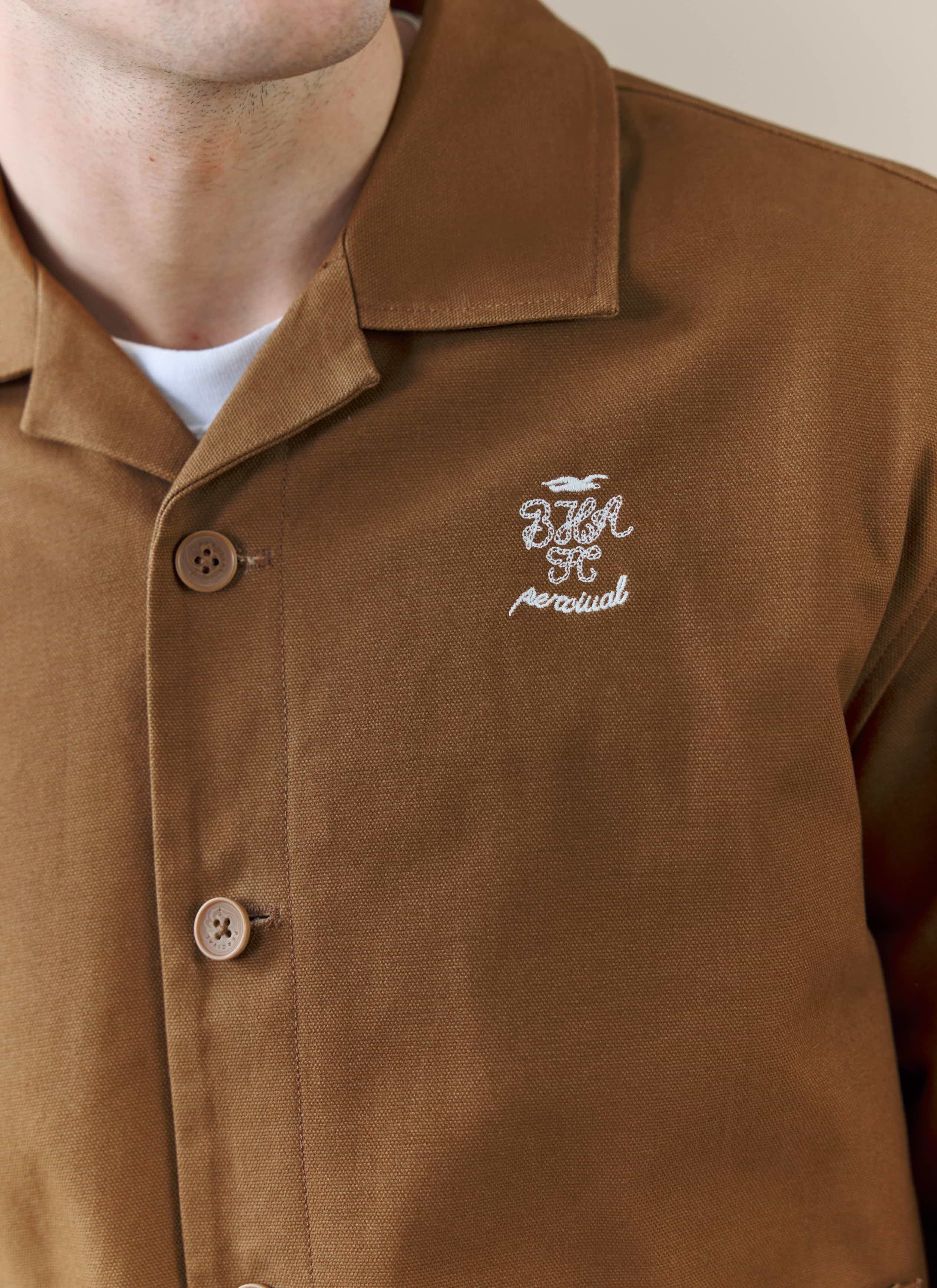 A close-up of the white embroidered logo on the chest of the Percival x Brighton & Hove Albion FC Canvas Workshirt in brown.