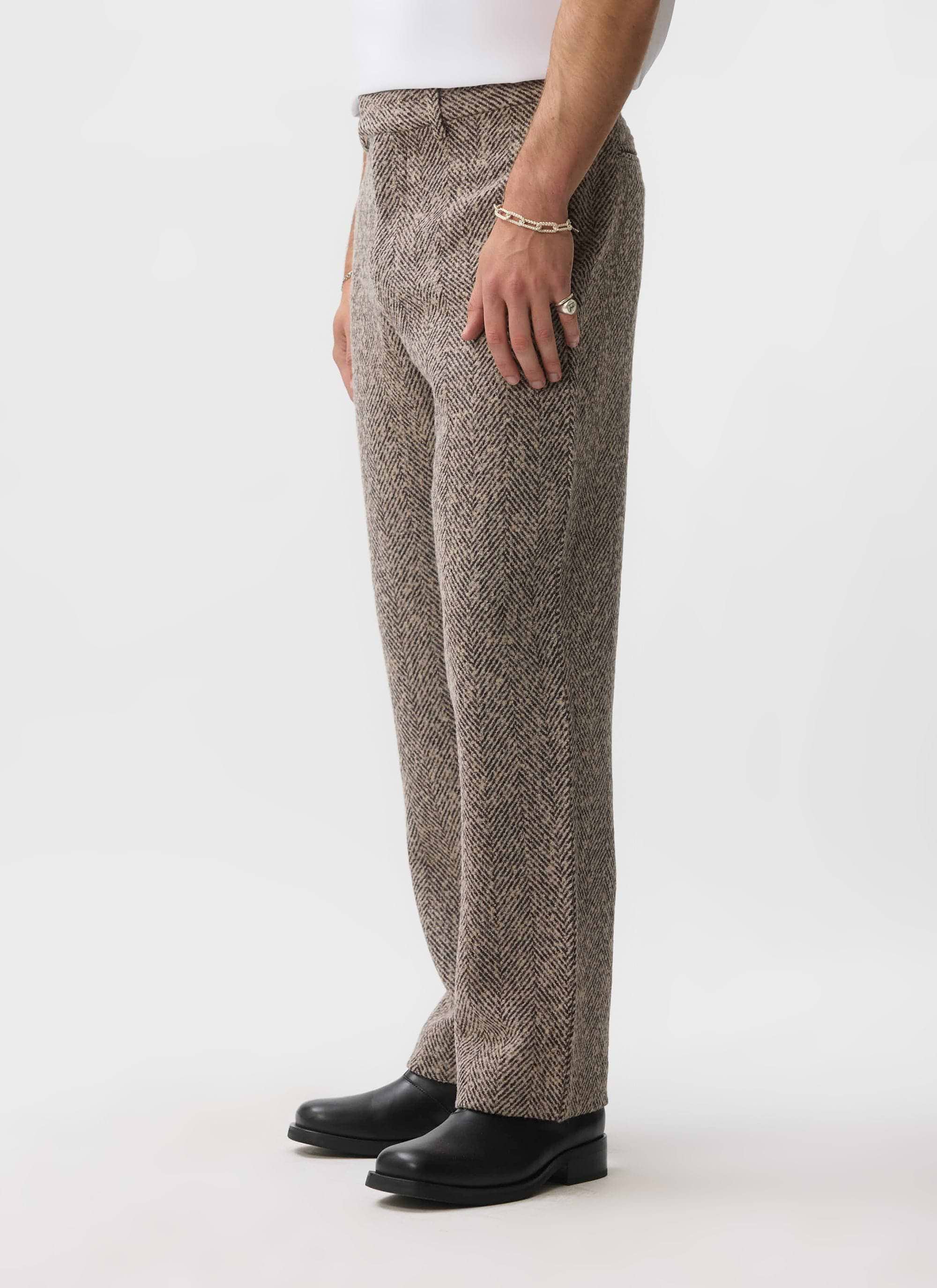 A model wears the Percival Herringbone Trousers in ecru, a side-on shot highlighting the straight leg wool-blend fit.