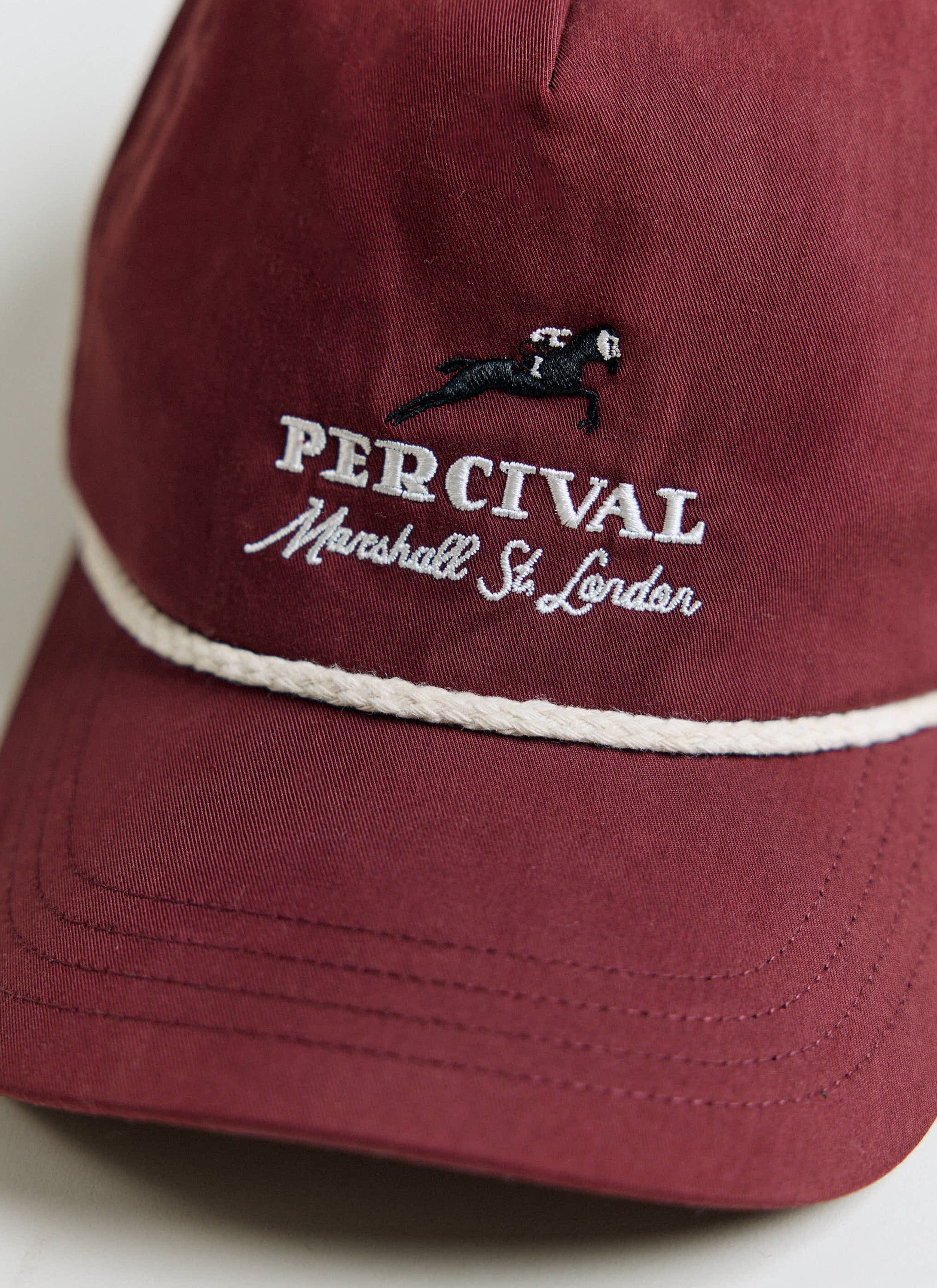 Close-up of the white Percival embroidery and rope detail on the red cotton Tournament Soft Trucker Cap.