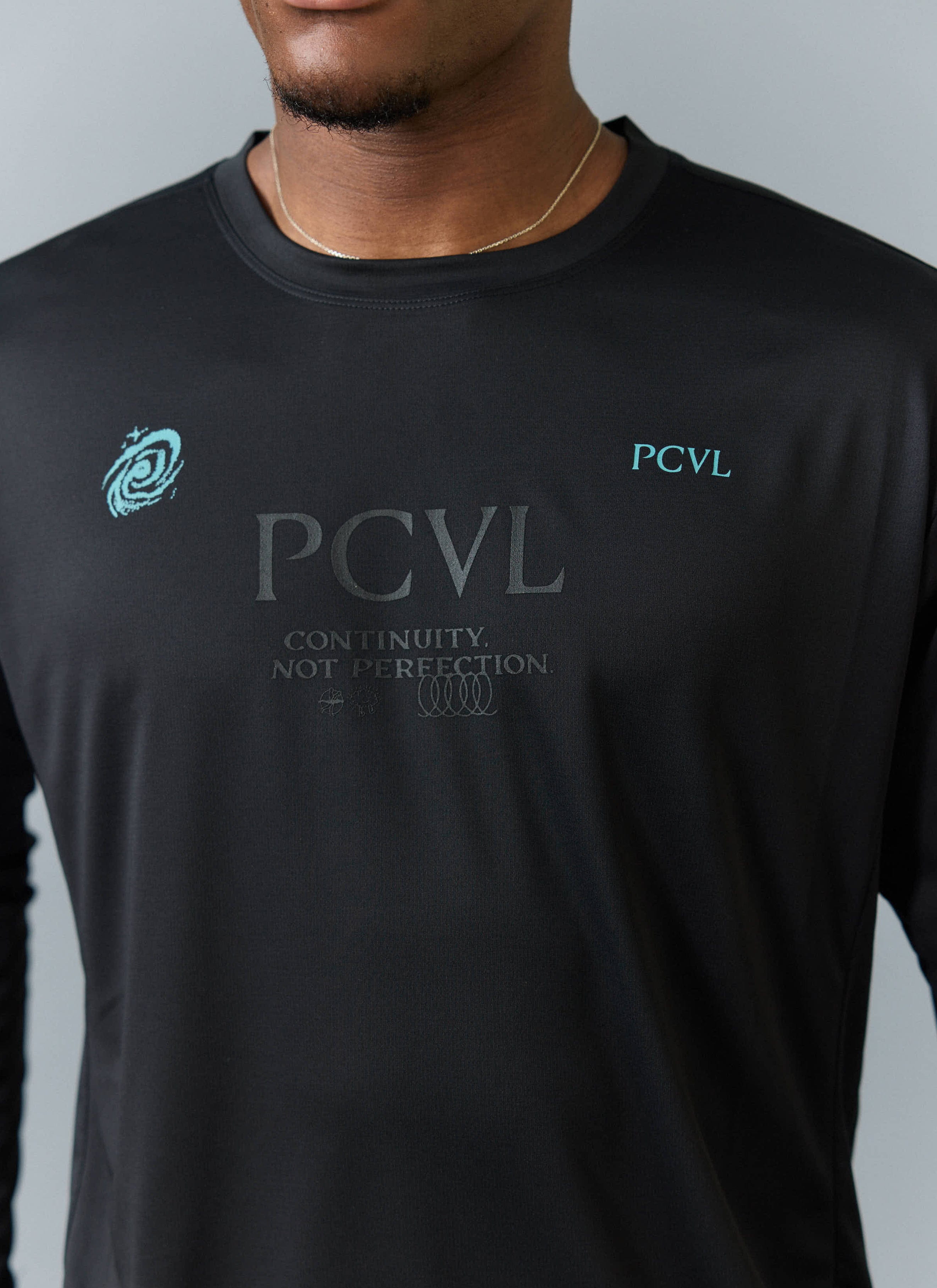 Close up of the Percival PCVL Long Sleeve Printed Performance Top in black, showing the tonal and turquoise chest graphics.