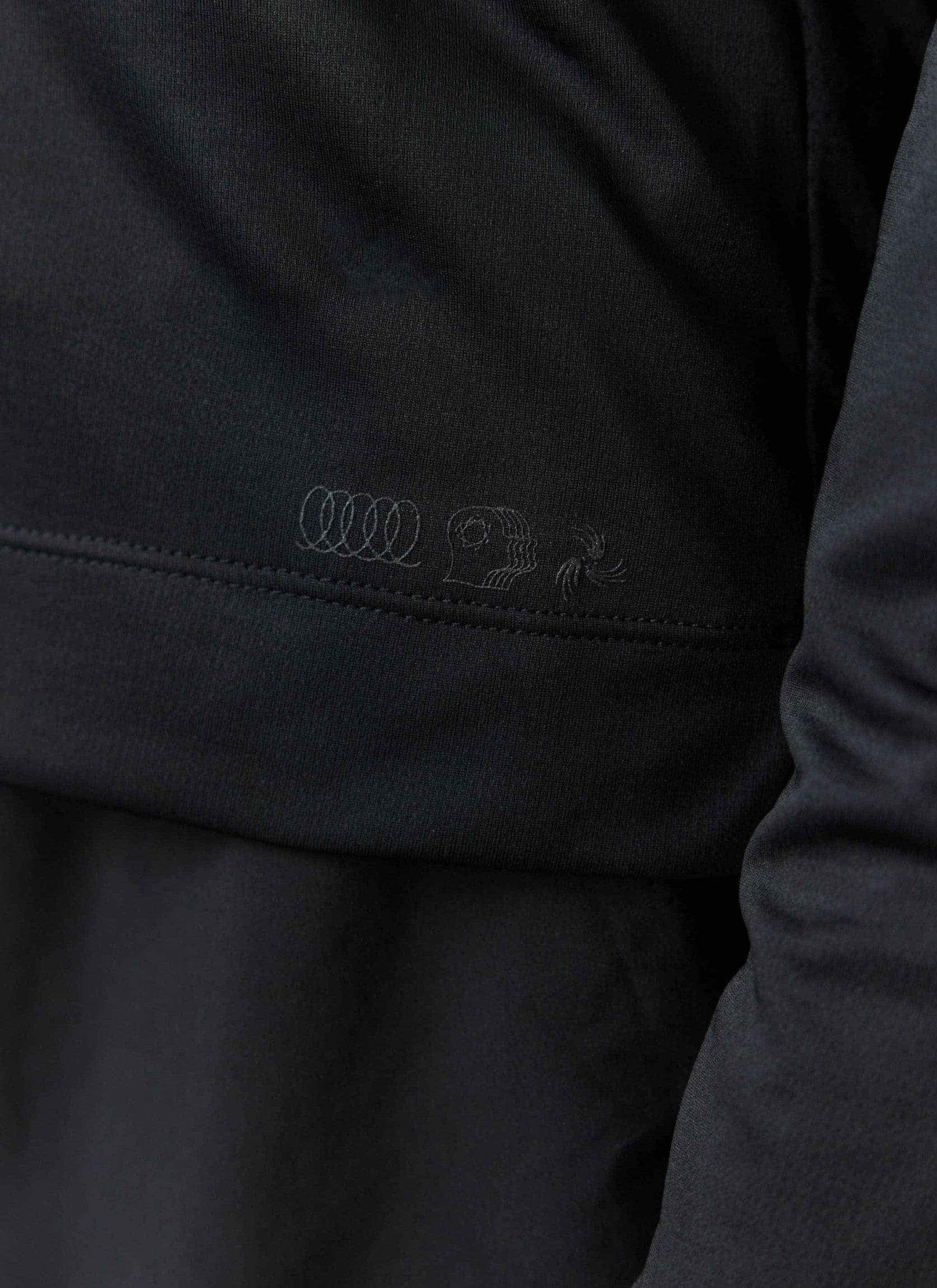 A close-up of the tonal PCVL graphic embroidered on the black Long Sleeve Performance Top by Percival.