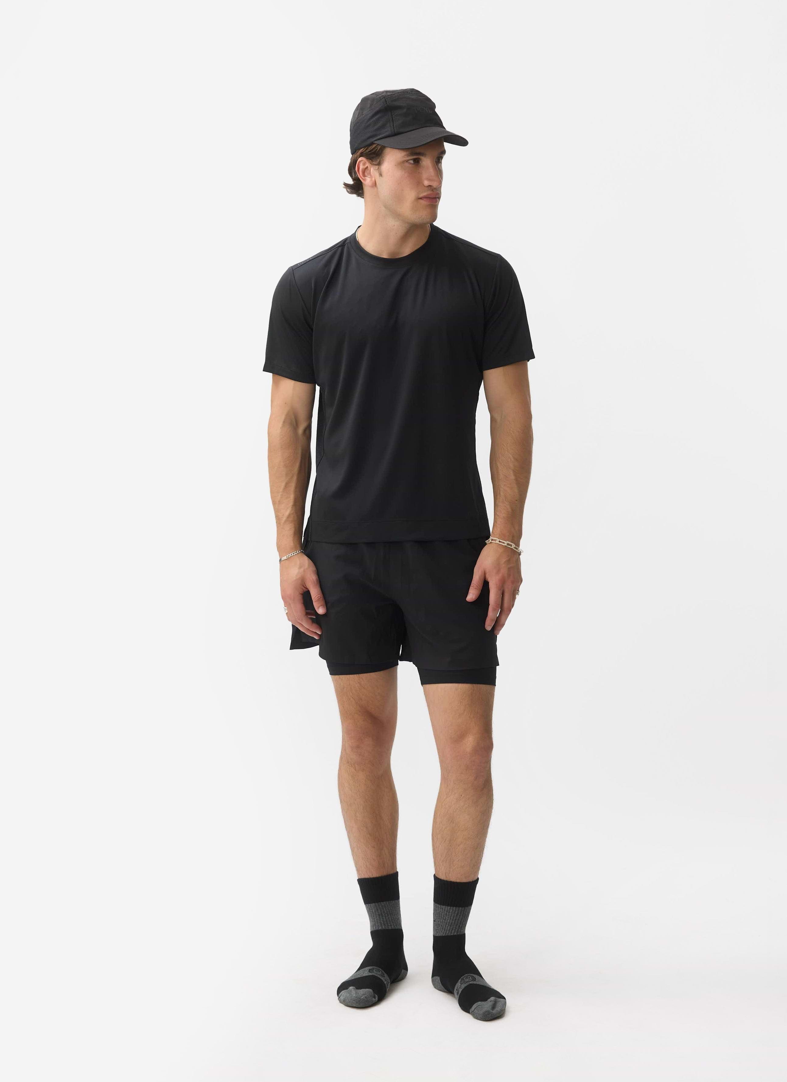 A model wears a full black activewear outfit from the Percival PCVL collection, including the Performance Top and socks.
