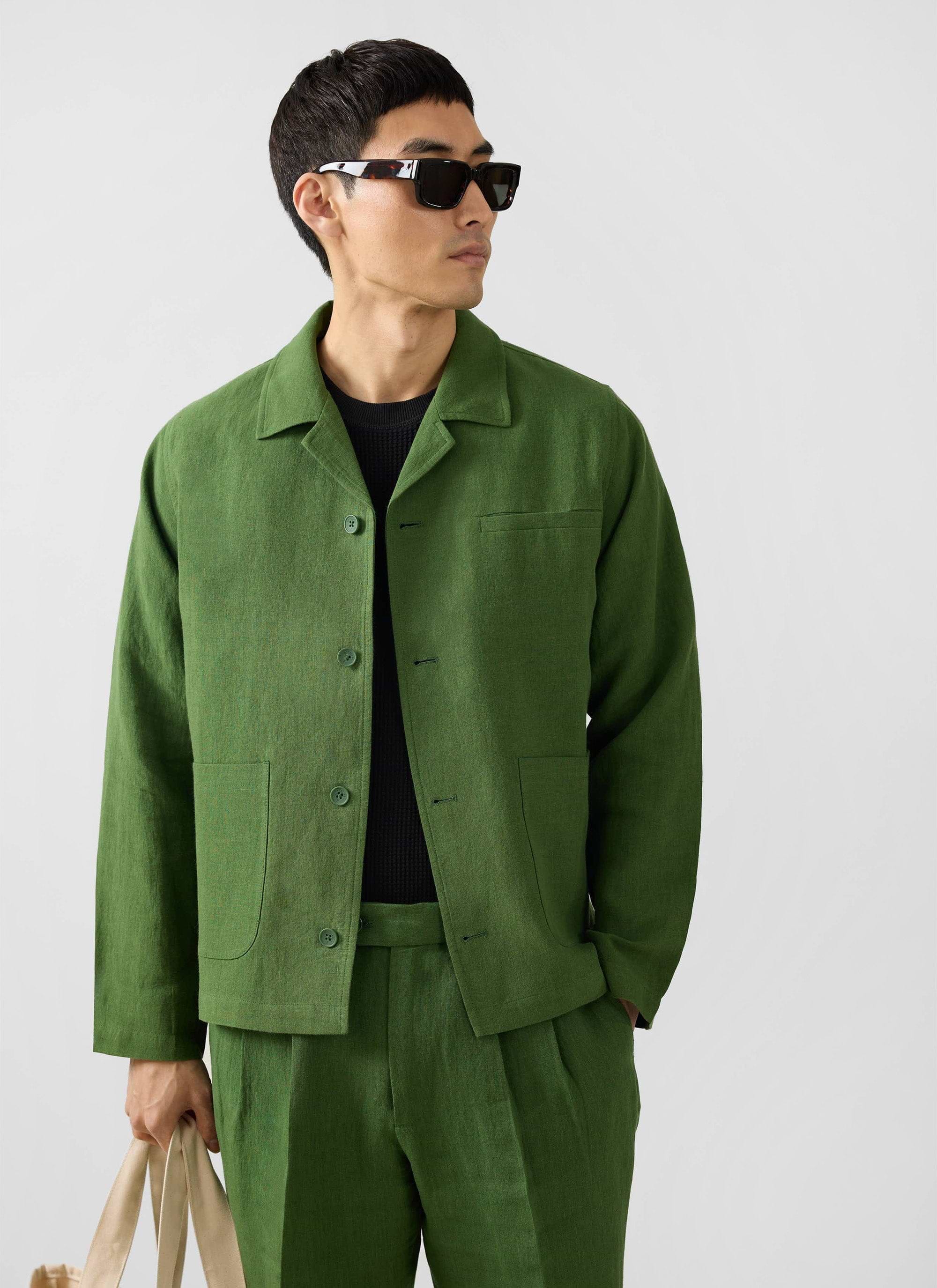 A model wears the Percival Linen Overshirt in Forest green as a suit with matching trousers, layered over a black knit.