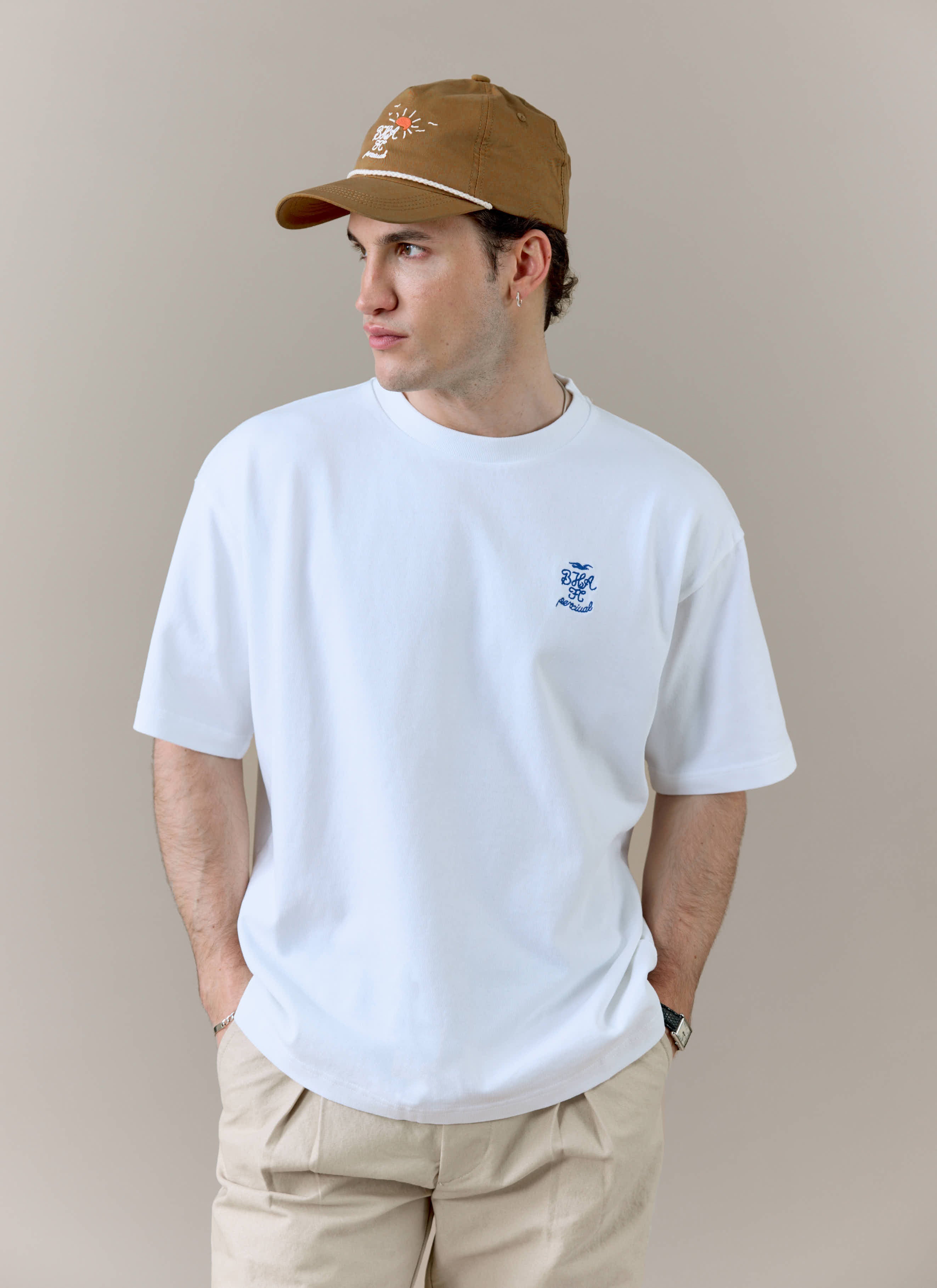 A model wears the white Percival x Brighton & Hove Albion F.C. tee, styled with beige trousers against a neutral background.