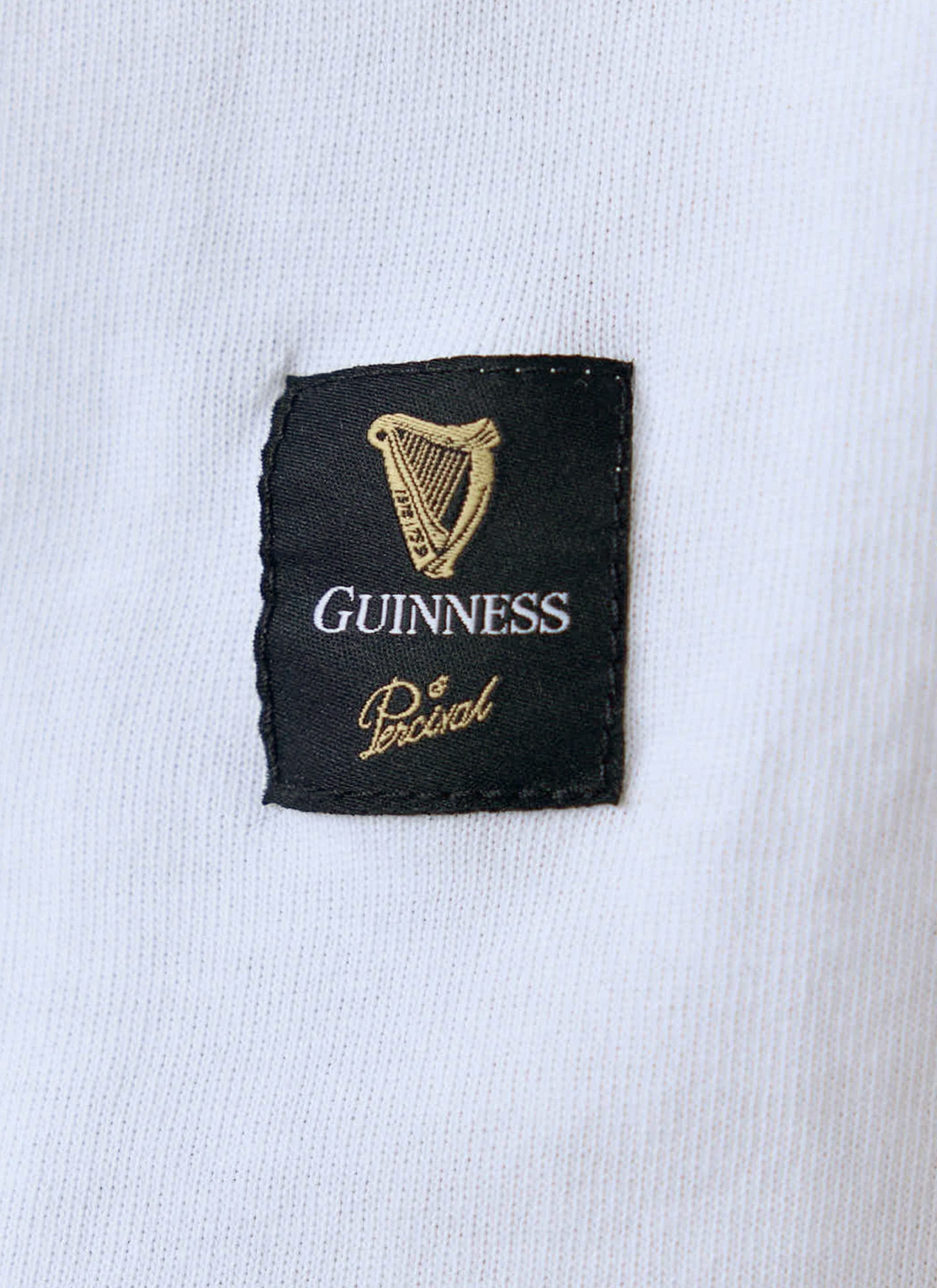A close-up of the black woven hem label featuring the Guinness and Percival logos on the white organic cotton t-shirt.