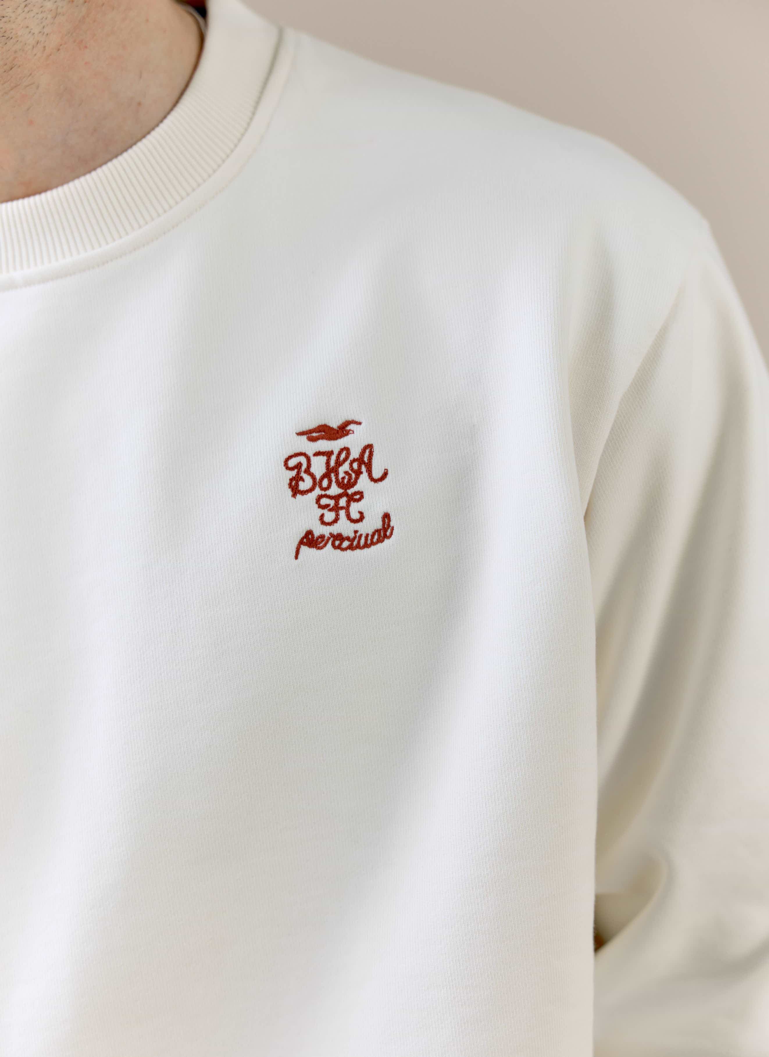 A detailed close-up of the embroidered chest logo on the cream Percival x Brighton & Hove Albion F.C. sweatshirt.