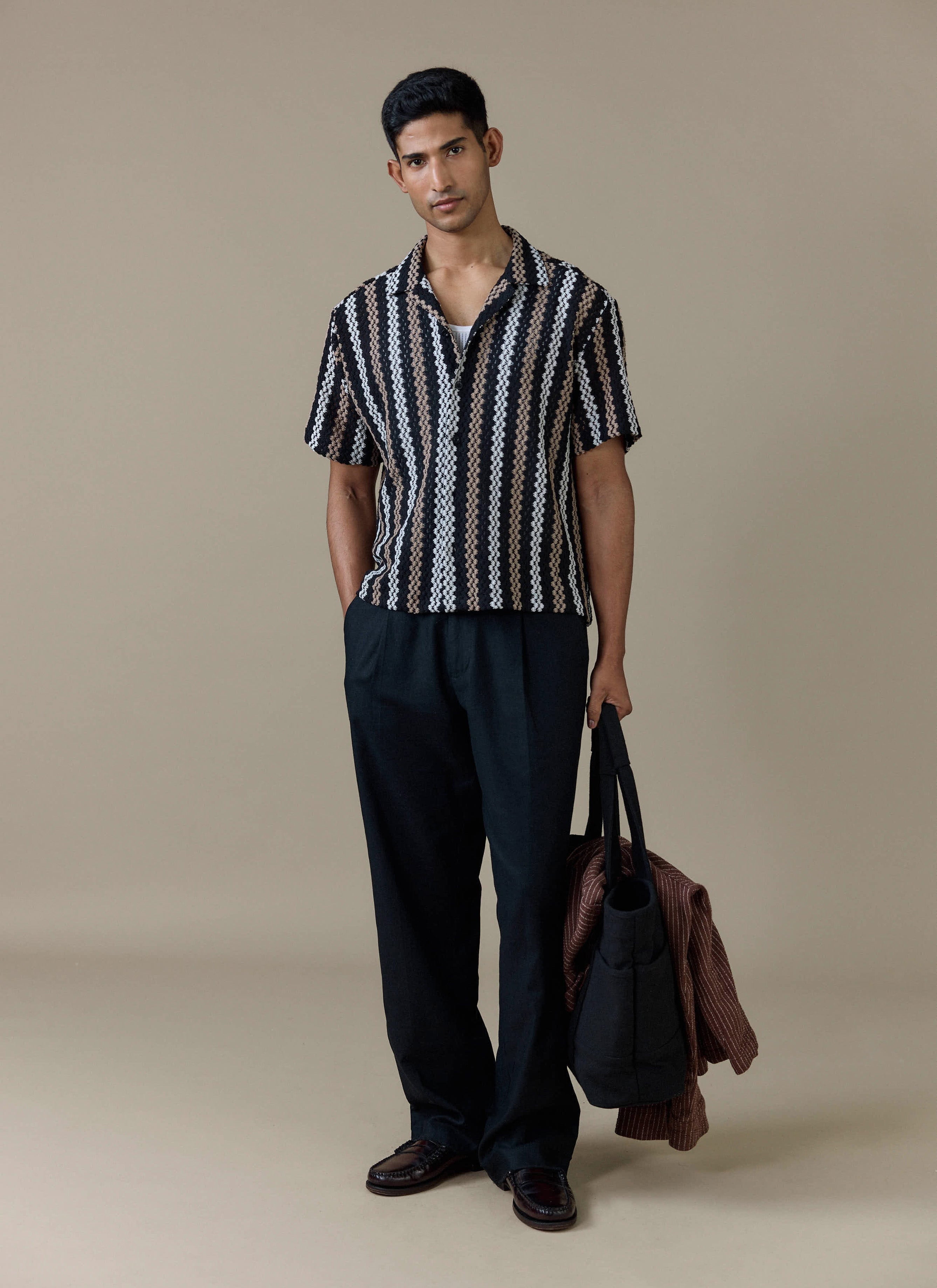 A model wears the Percival Wade Crochet Boxy Shirt in black with vertical stripes, styled with black trousers.