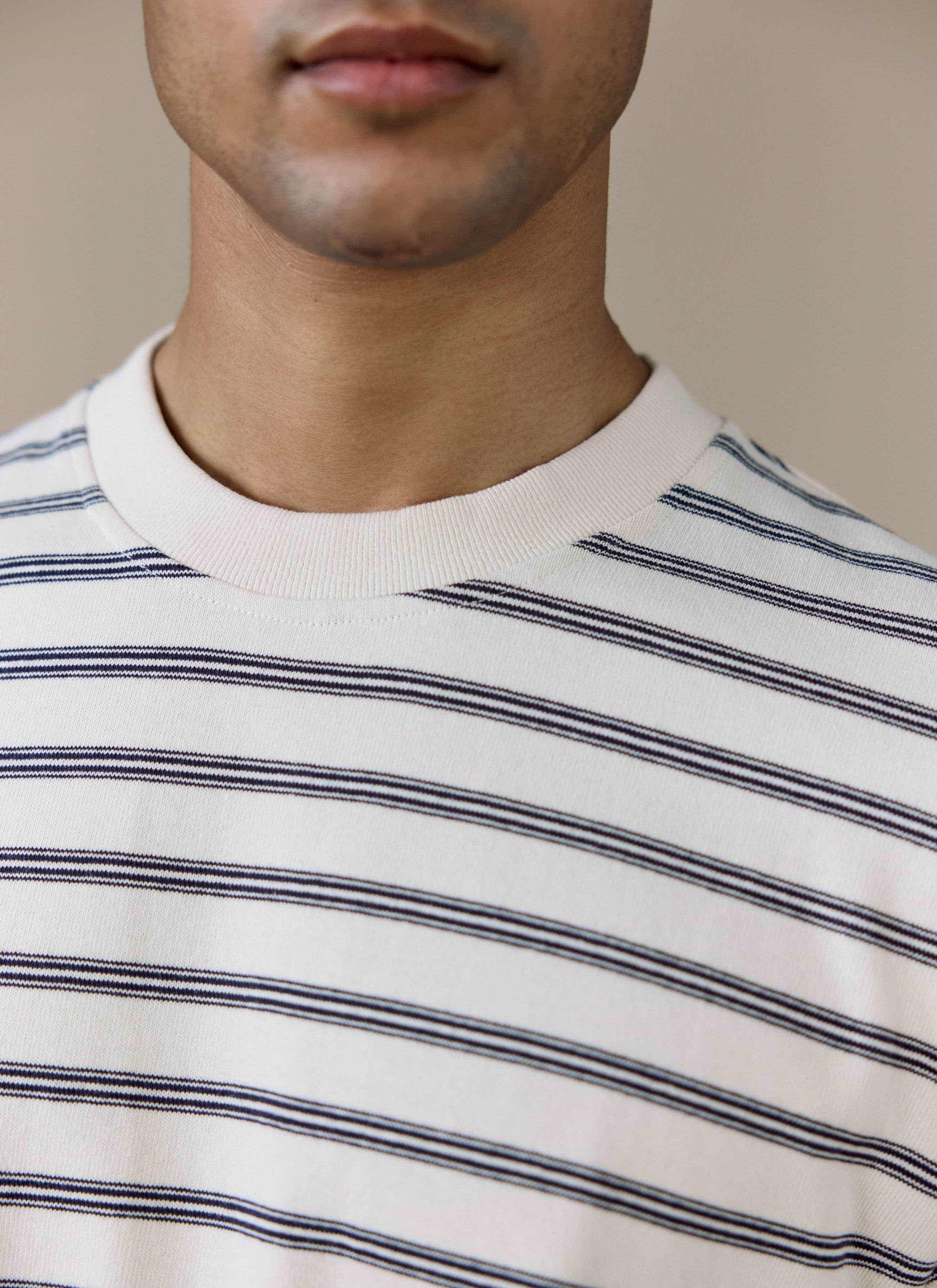 Close-up of a model wearing the Percival Arlo Raw Hem Breton T Shirt in white stripe, showing the ribbed crew neck.
