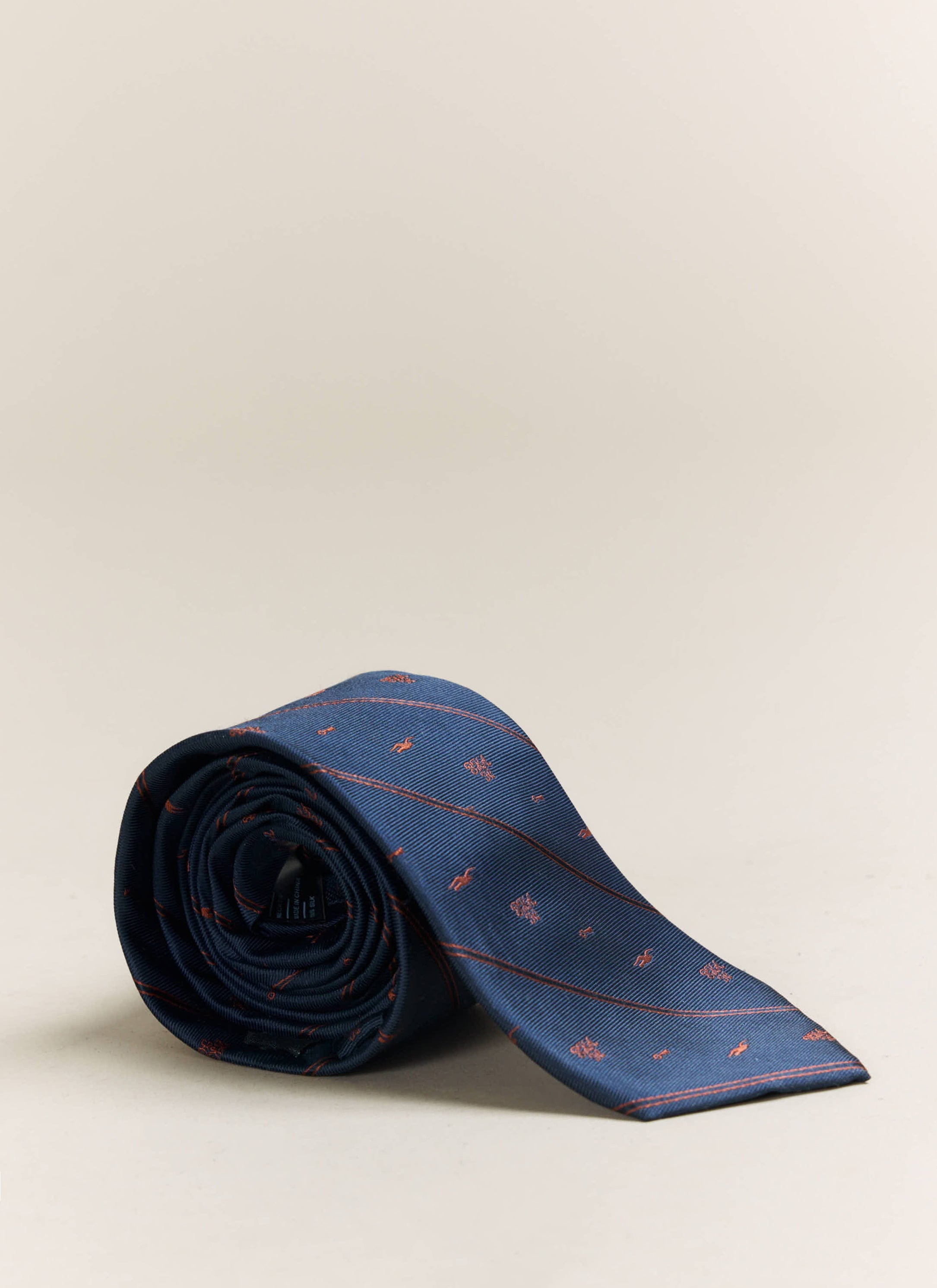 A studio shot of the Percival x Brighton & Hove Albion F.C. navy silk tie, rolled to display the orange jacquard pattern.