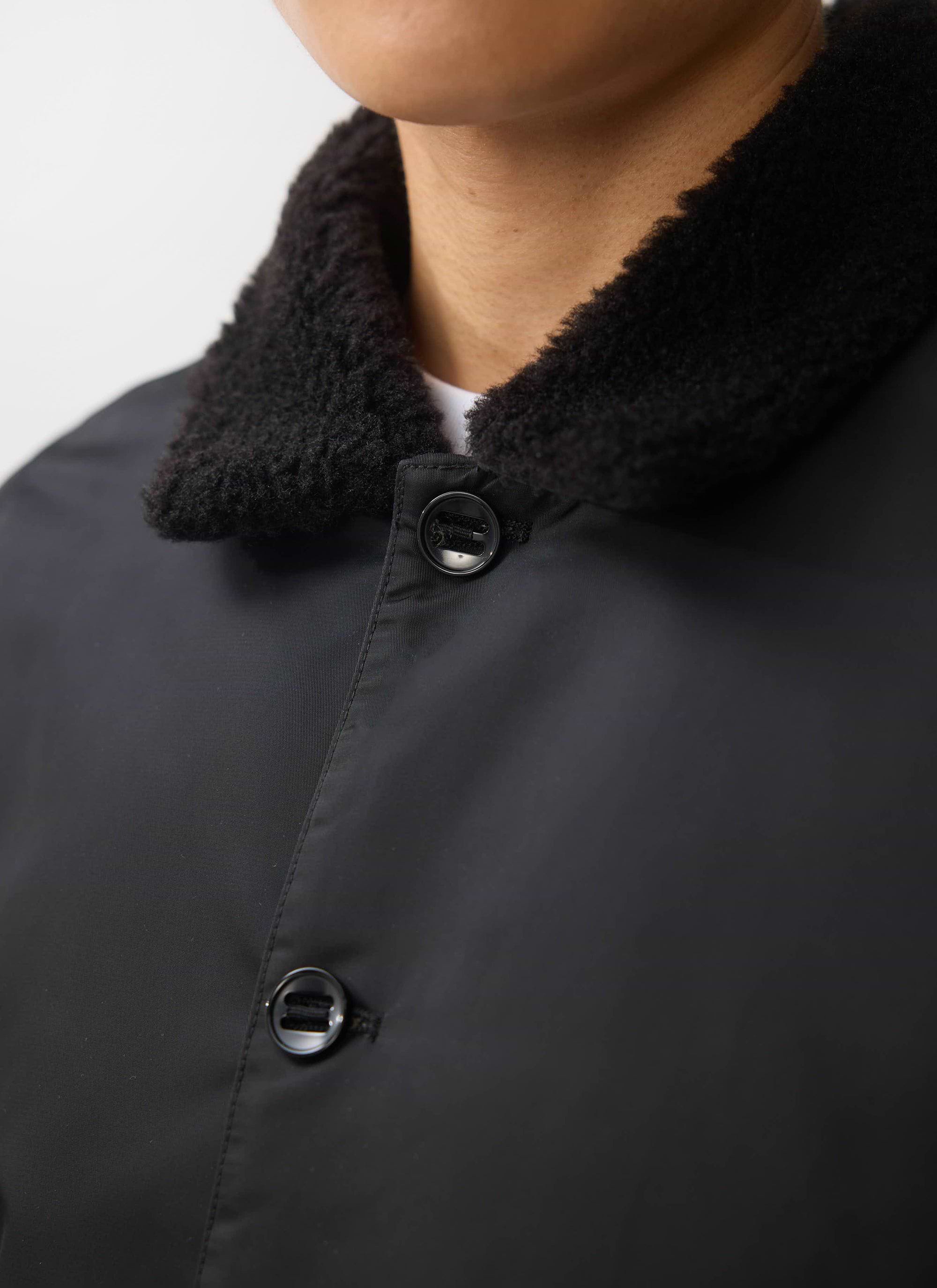 A close-up of the Percival Doppio Bomber Jacket in black, showing the faux shearling collar and button detail.