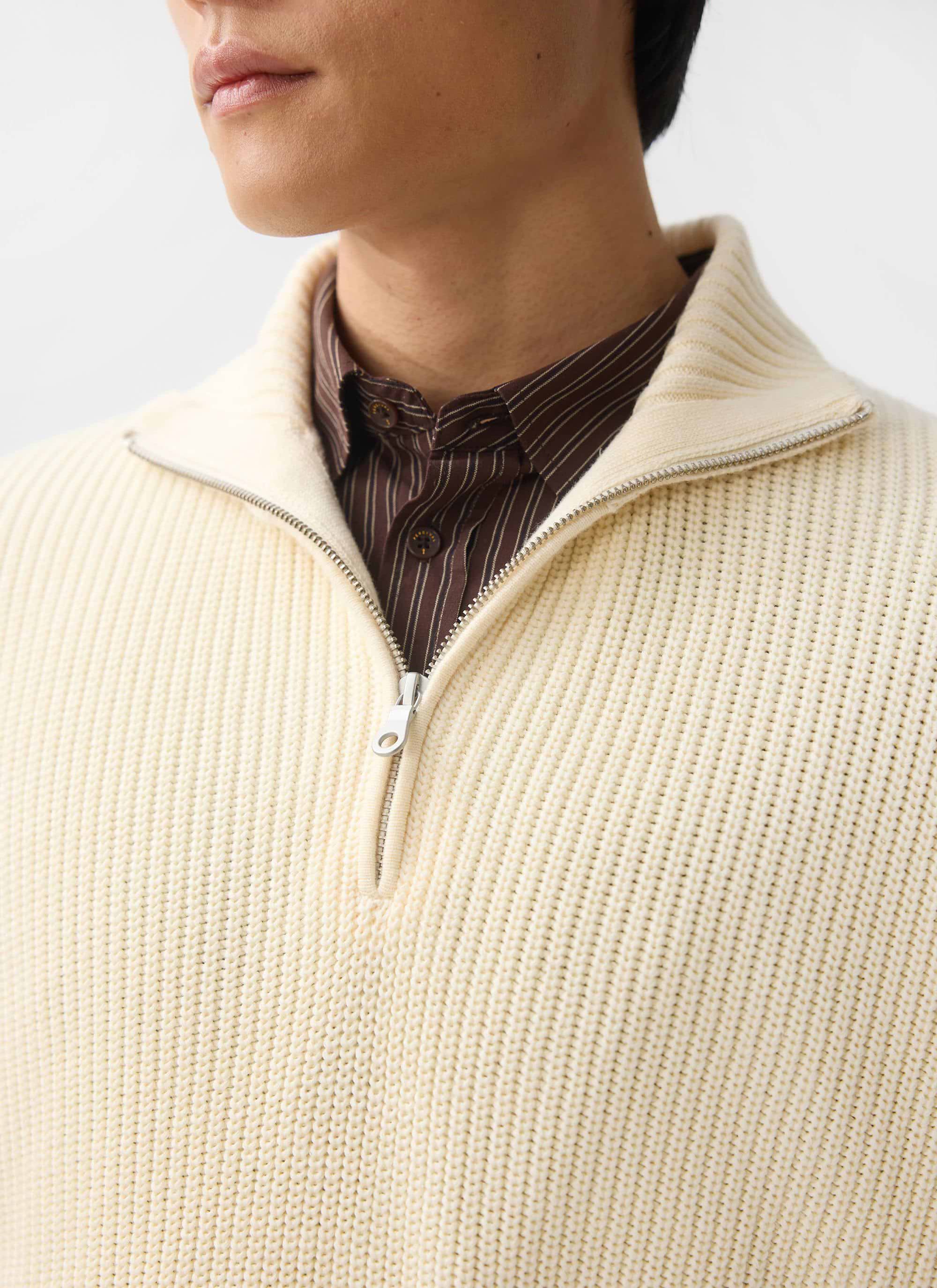 A close-up of a model wearing the Percival Meyer Quarter Zip Fisherman jumper in ecru, layered over a brown striped shirt.