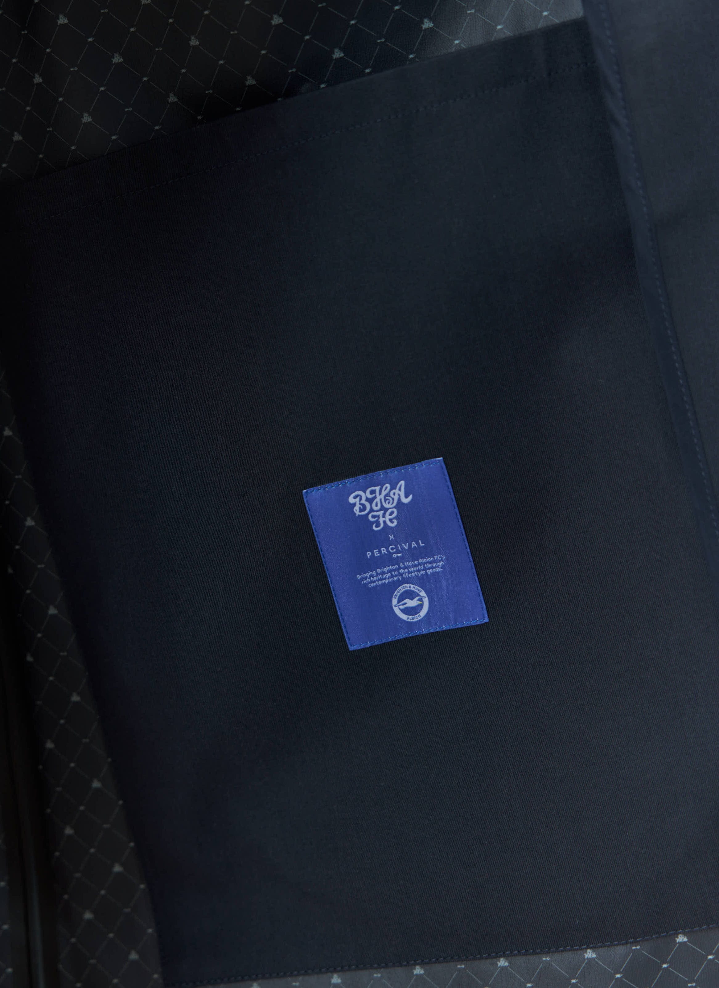 Close-up detail of the Percival x Brighton & Hove Albion FC Sherlock Trench, showing the internal label and patterned lining.